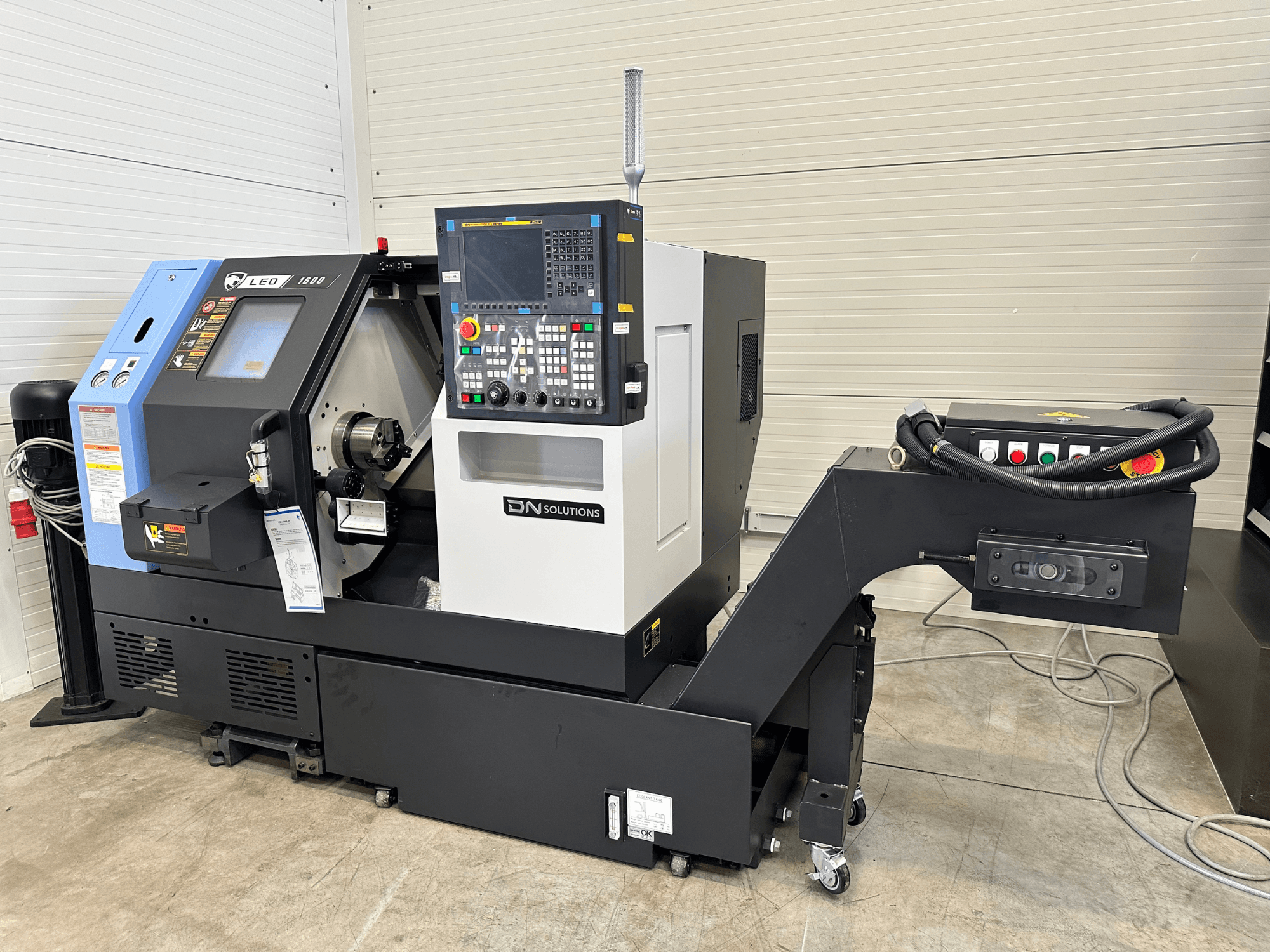 Vista frontal do centro de torneamento-fresagem Leo 1600 da DN SOLUTIONS, com painel de controlo digital e suporte de ferramentas, sobre uma base preta.