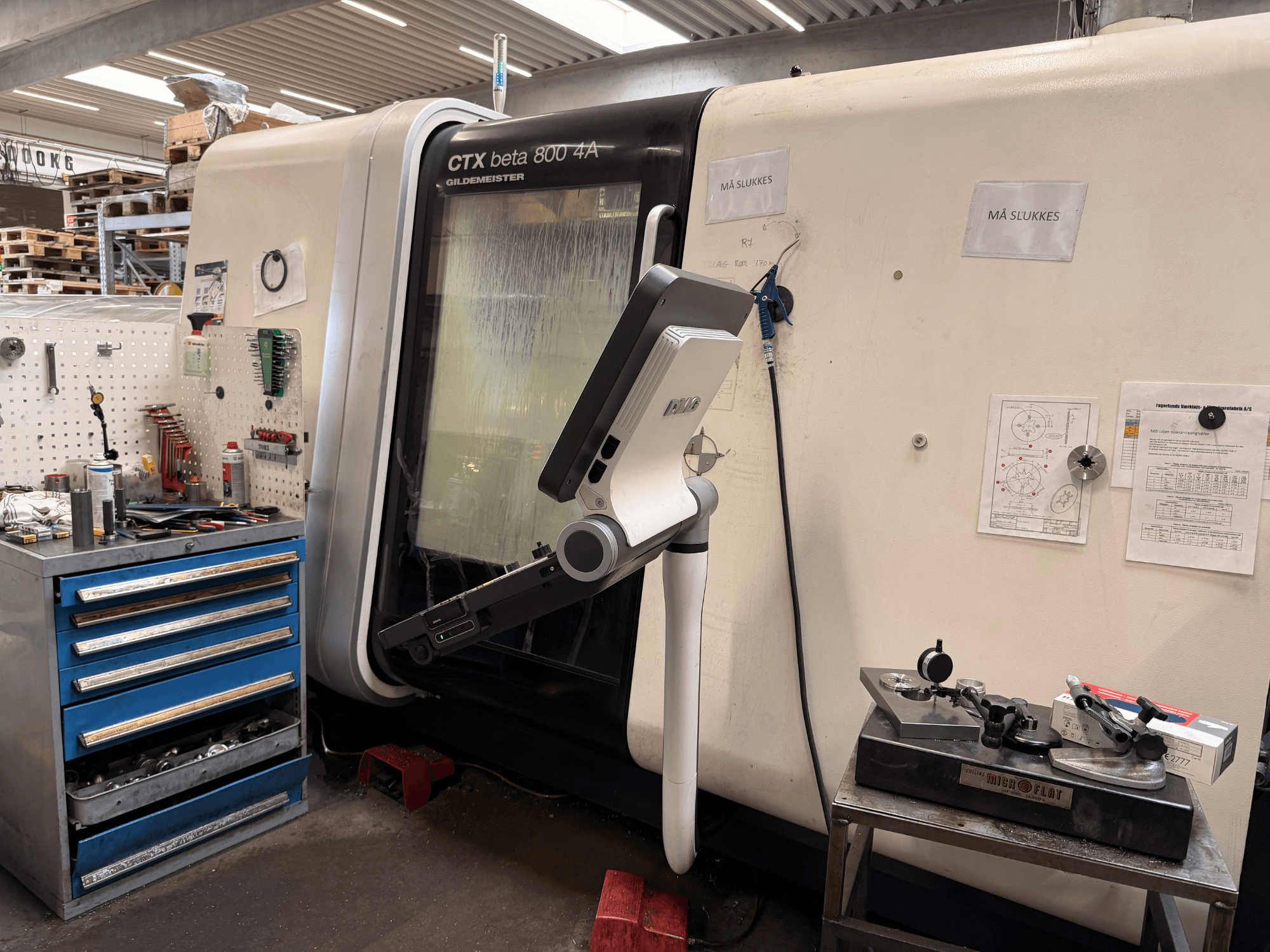 O torno vertical DMG MORI CTX Beta 800 4a numa oficina, com um braço de comando e documentos técnicos nas proximidades.