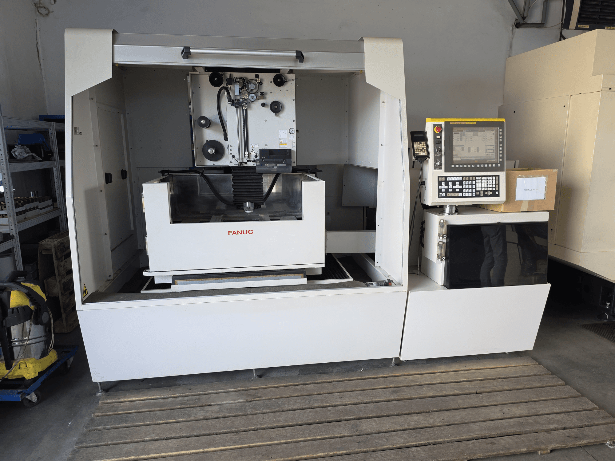 Máquina de electroerosão por fio FANUC ROBOCUT alpha-1iD, vista frontal que mostra o painel de controlo, a área de trabalho e o design compacto num ambiente de oficina.