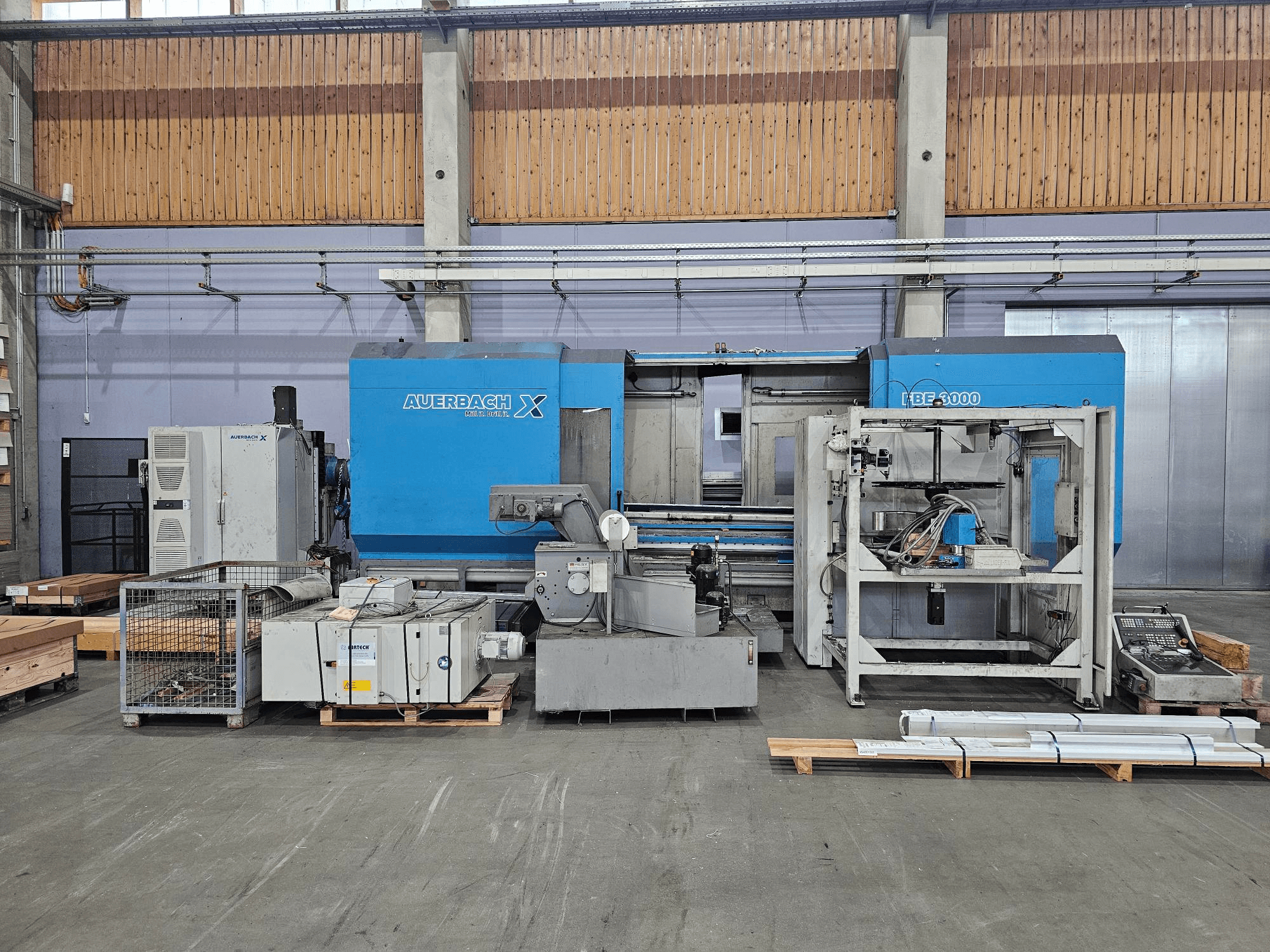 Máquina Auerbach X LBF-3000 em ambiente de fábrica, vista lateral, com componentes cinzentos e azuis e painel de controlo visível.