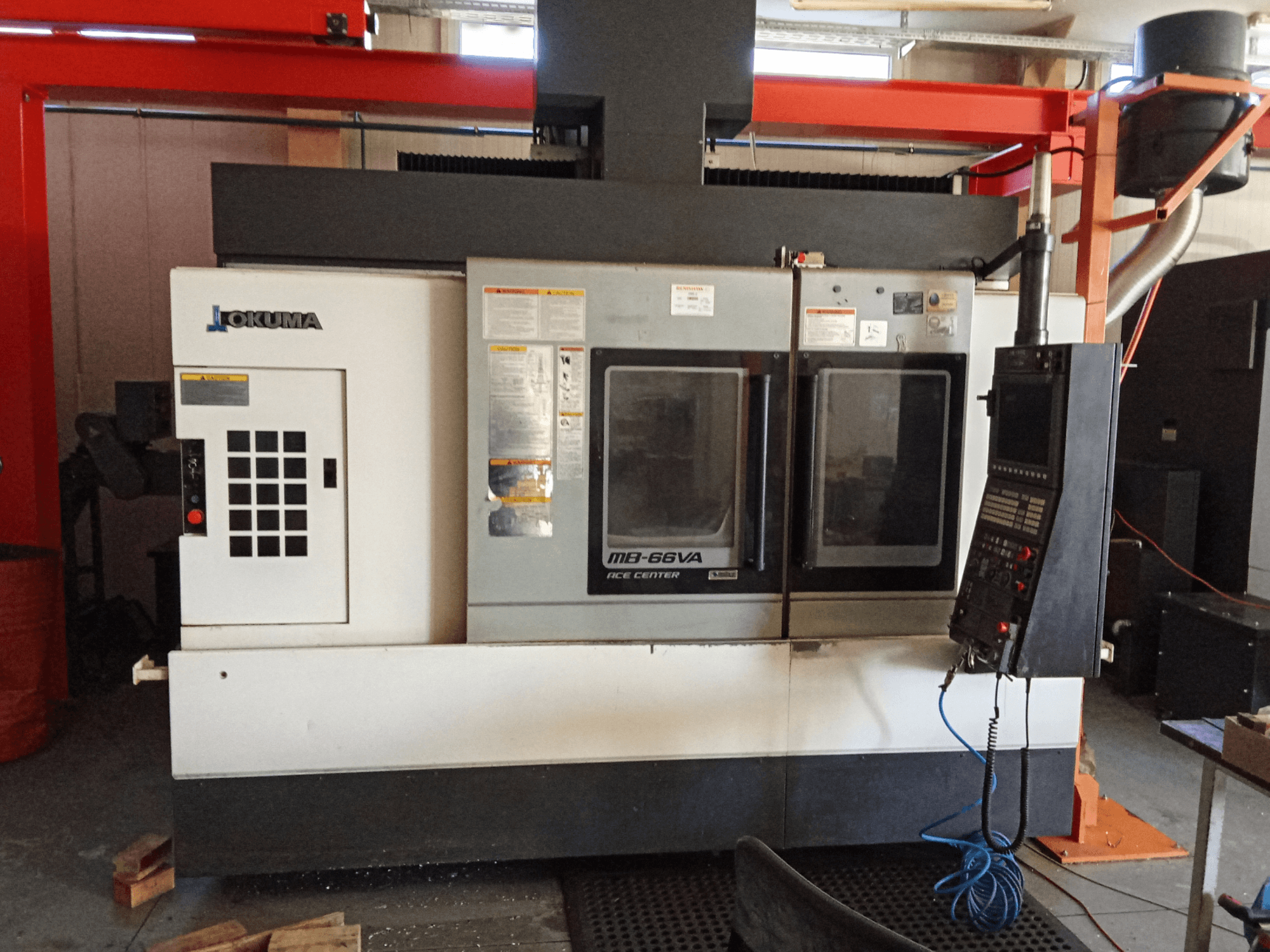 Centro de maquinação vertical Okuma MB-66VA, vista frontal mostrando o painel de controlo e as janelas de visualização dupla para acesso às ferramentas.