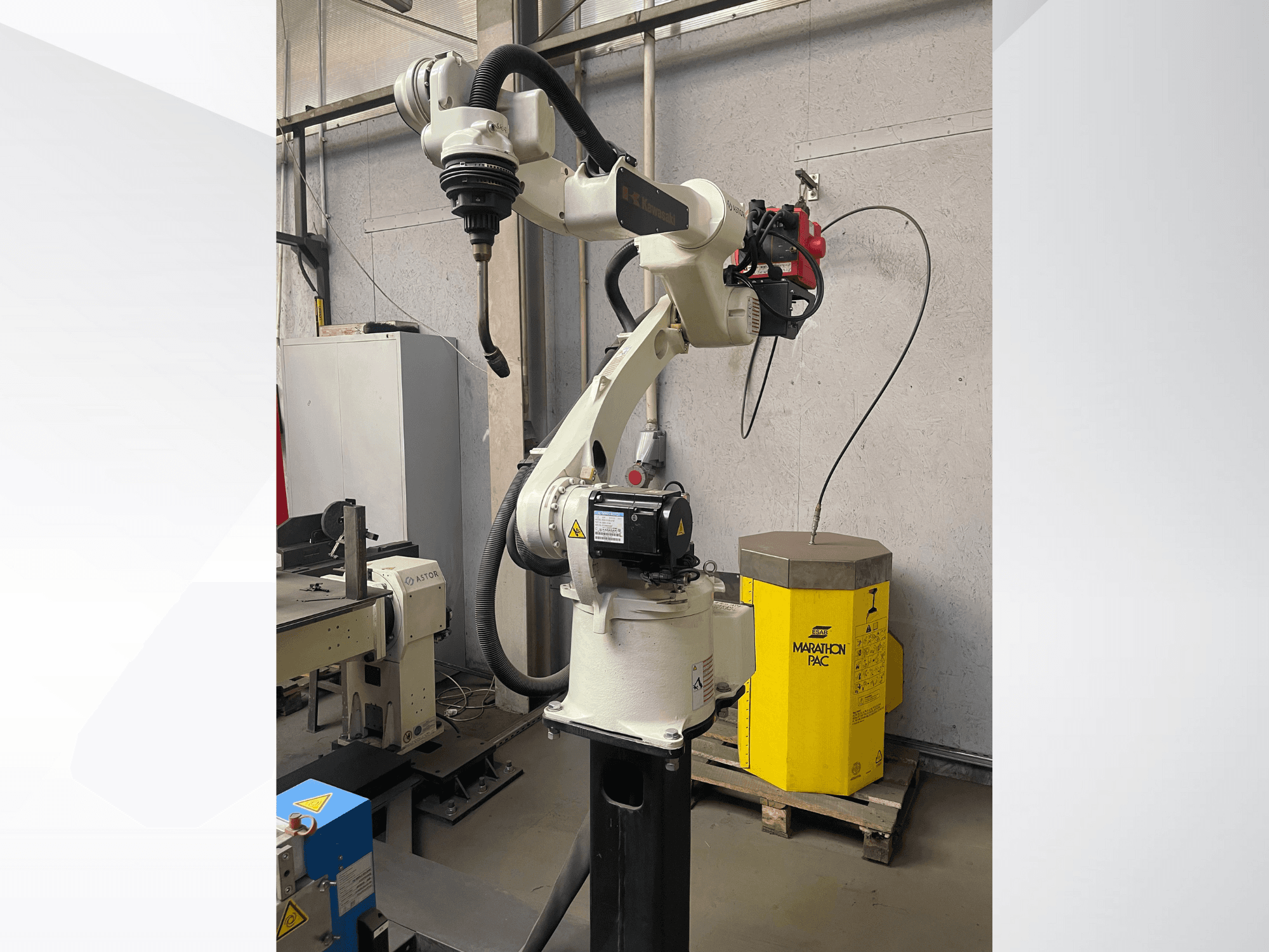 Braço robótico Kawasaki numa vista lateral, com um suporte de ferramentas montado, com uma unidade de potência amarela em segundo plano.