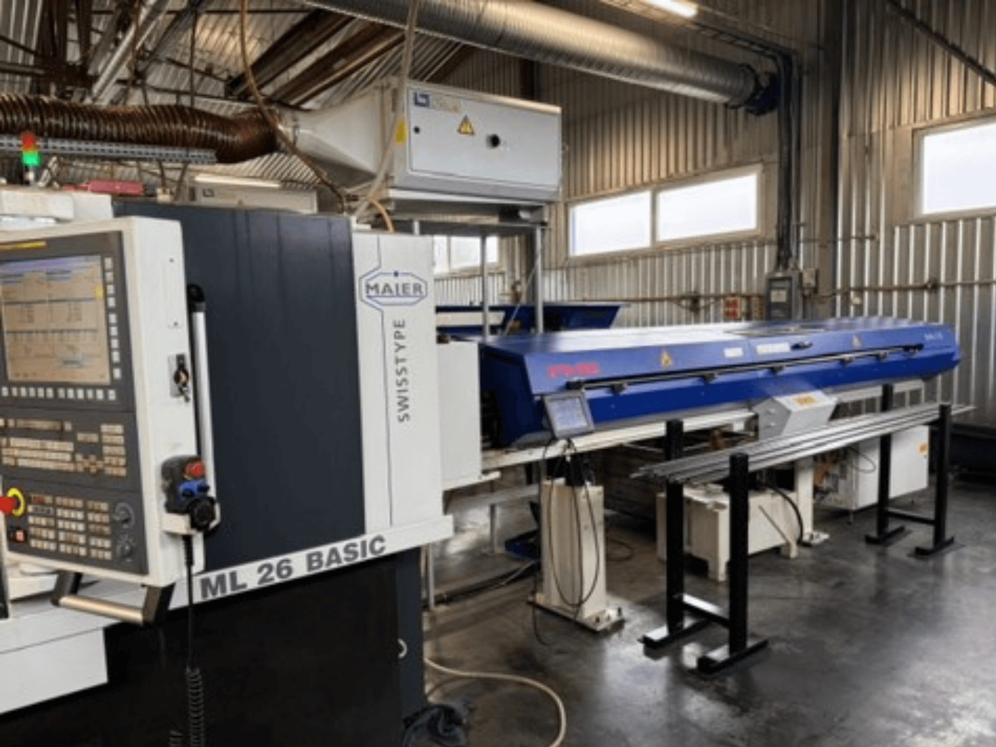Texto alternativo: Vista frontal da máquina de torneamento Maier ML26 C5Y Swiss Type, com painel de controlo e dispositivo azul acoplado, num ambiente industrial.