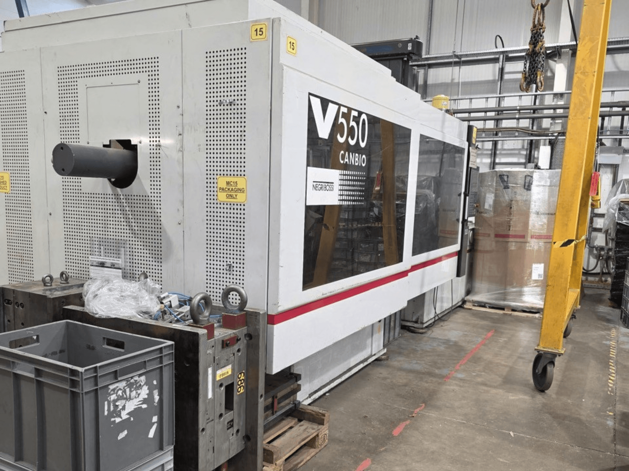 Máquina de moldagem por injeção hidráulica Negri Bossi V55000H-4250, vista lateral, com painel de controlo e caixas cinzentas em primeiro plano.