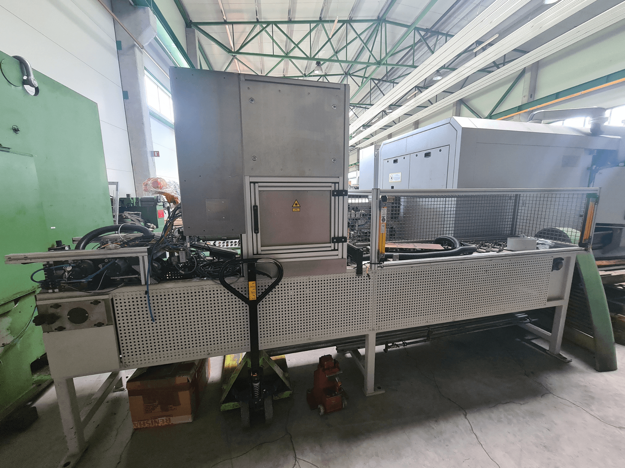 Máquinas industriais com uma estrutura metálica, mangueiras e painel de controlo, vistas de lado numa fábrica.