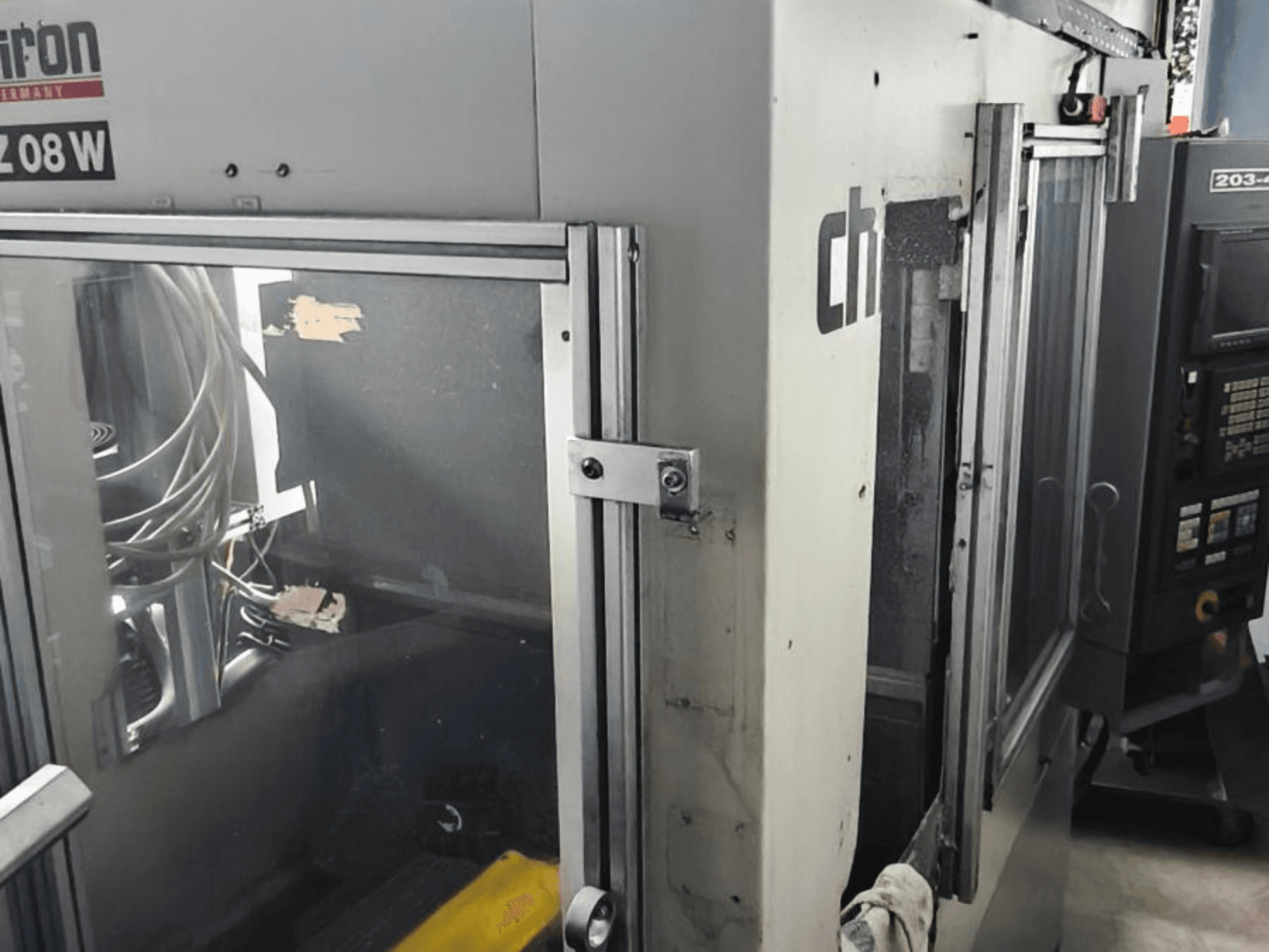 Centro de maquinação vertical CHIRON FZ 08 W, vista frontal mostrando painel de controlo e portas parcialmente abertas, com componentes internos visíveis.