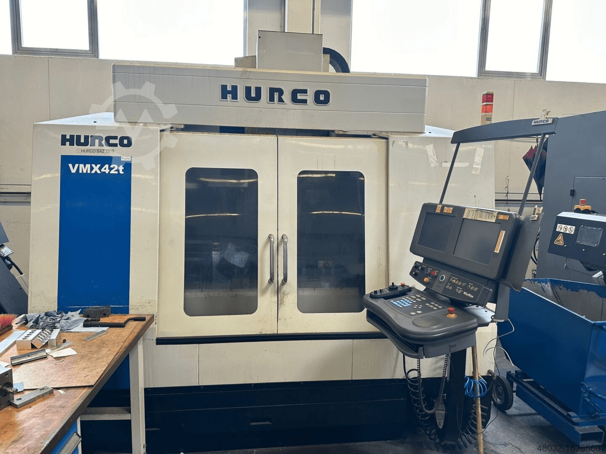Centro de usinagem vertical Hurco VMX42t, vista frontal, mostrando o painel de controlo e o interior visível com ferramentas e peças de trabalho.