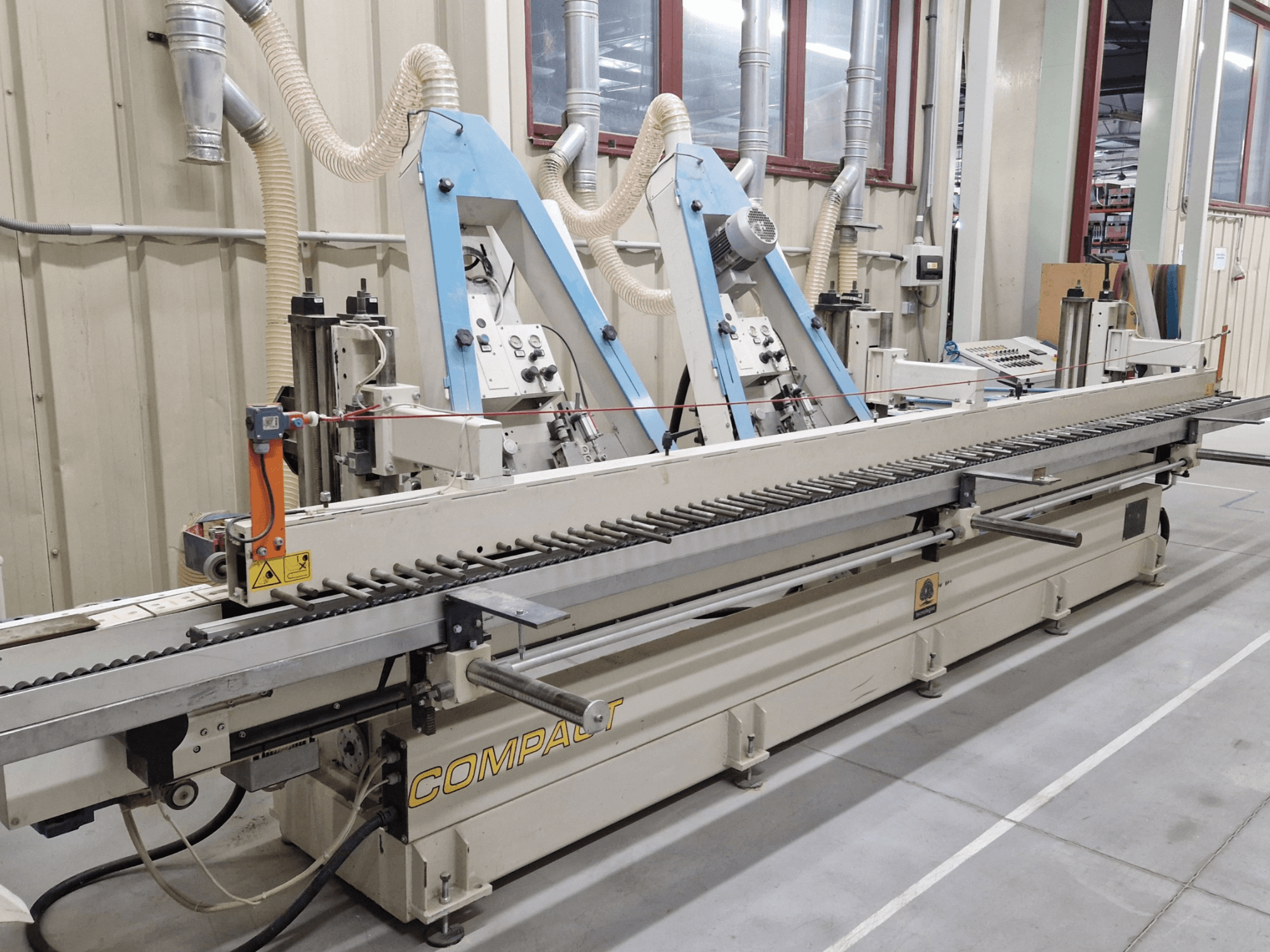 Lixadeira de cinta TECNOLEGNO COMPACT 52 numa oficina, mostrando o painel de controlo e o mecanismo da cinta de lixa de um ponto de vista lateral.