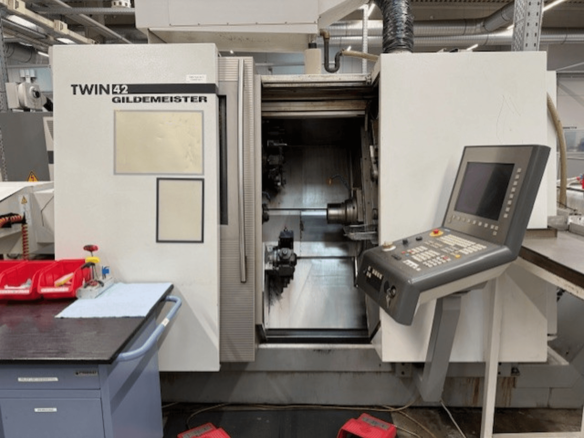 Torno horizontal Gildemeister TWIN 42; vista frontal que mostra o painel de controlo e a câmara do fuso aberta.