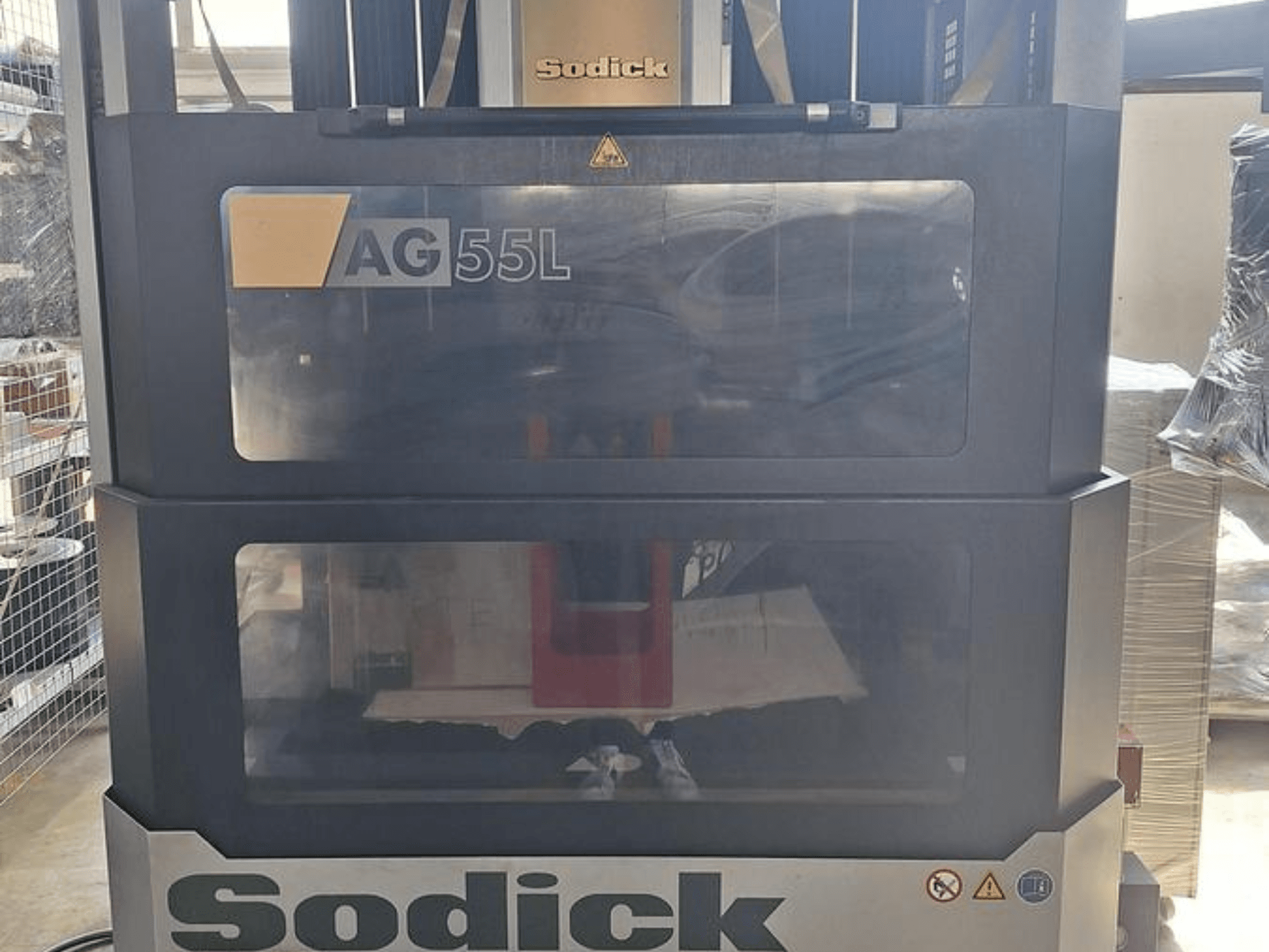 Sodick AG 55L Die-Sinking EDM Machine, vista frontal com controlos visíveis através de painéis transparentes, mostrando o espaço de trabalho no interior.