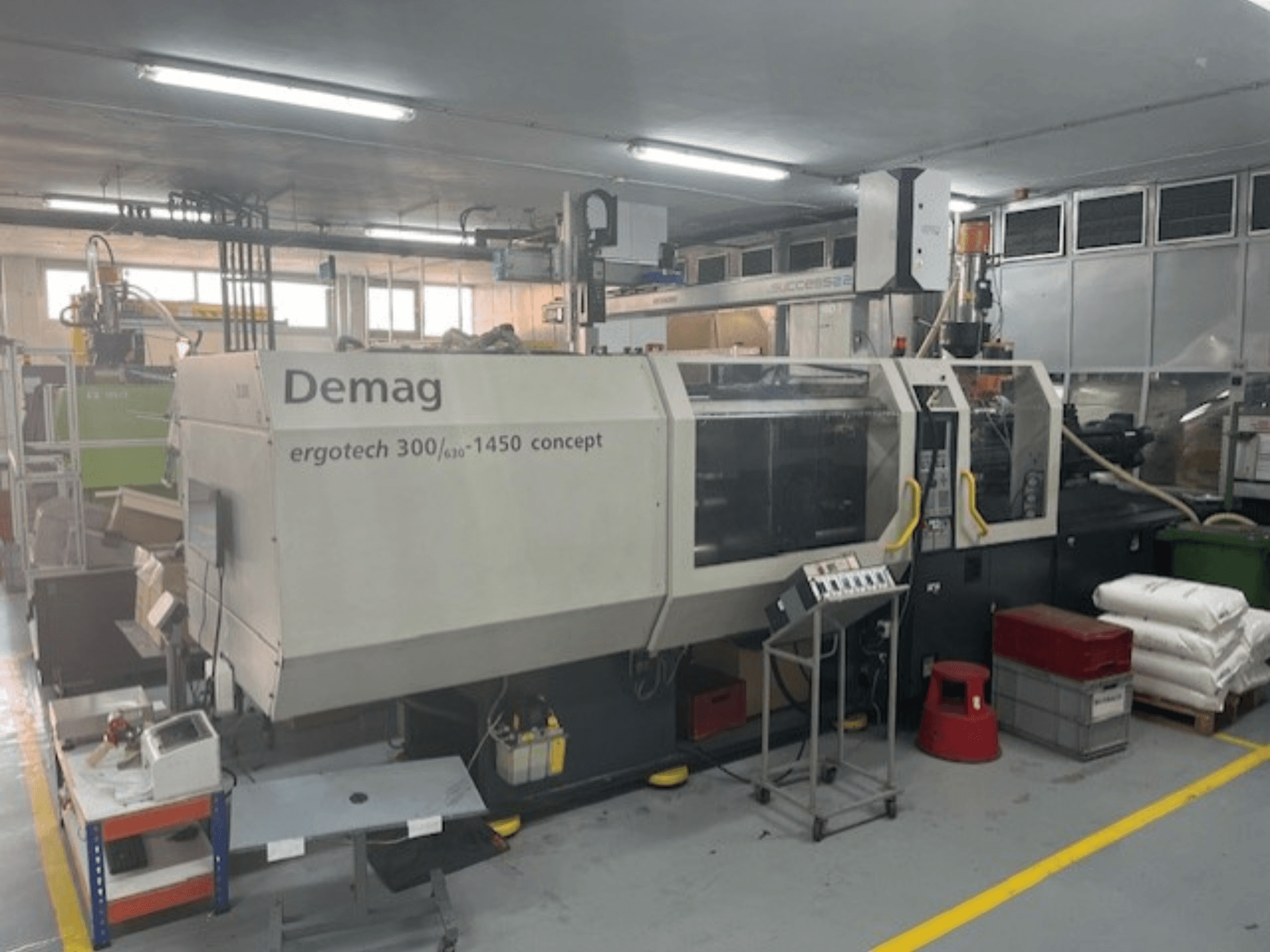 Máquina de moldagem por injeção hidráulica Demag ERGOTECH CONCEPT 3000-1450, vista frontal, com controlos operacionais e materiais próximos.