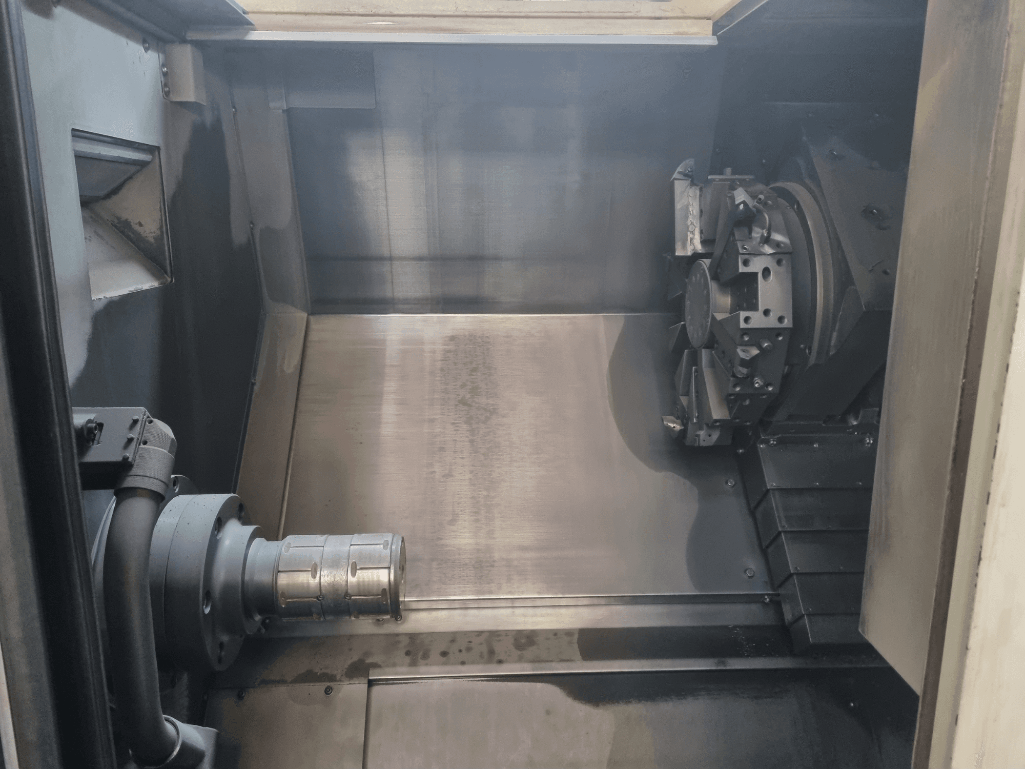 Vista interior de uma máquina CNC mostrando uma área de trabalho em metal, suporte de ferramentas e mandril; realça a engenharia de precisão.