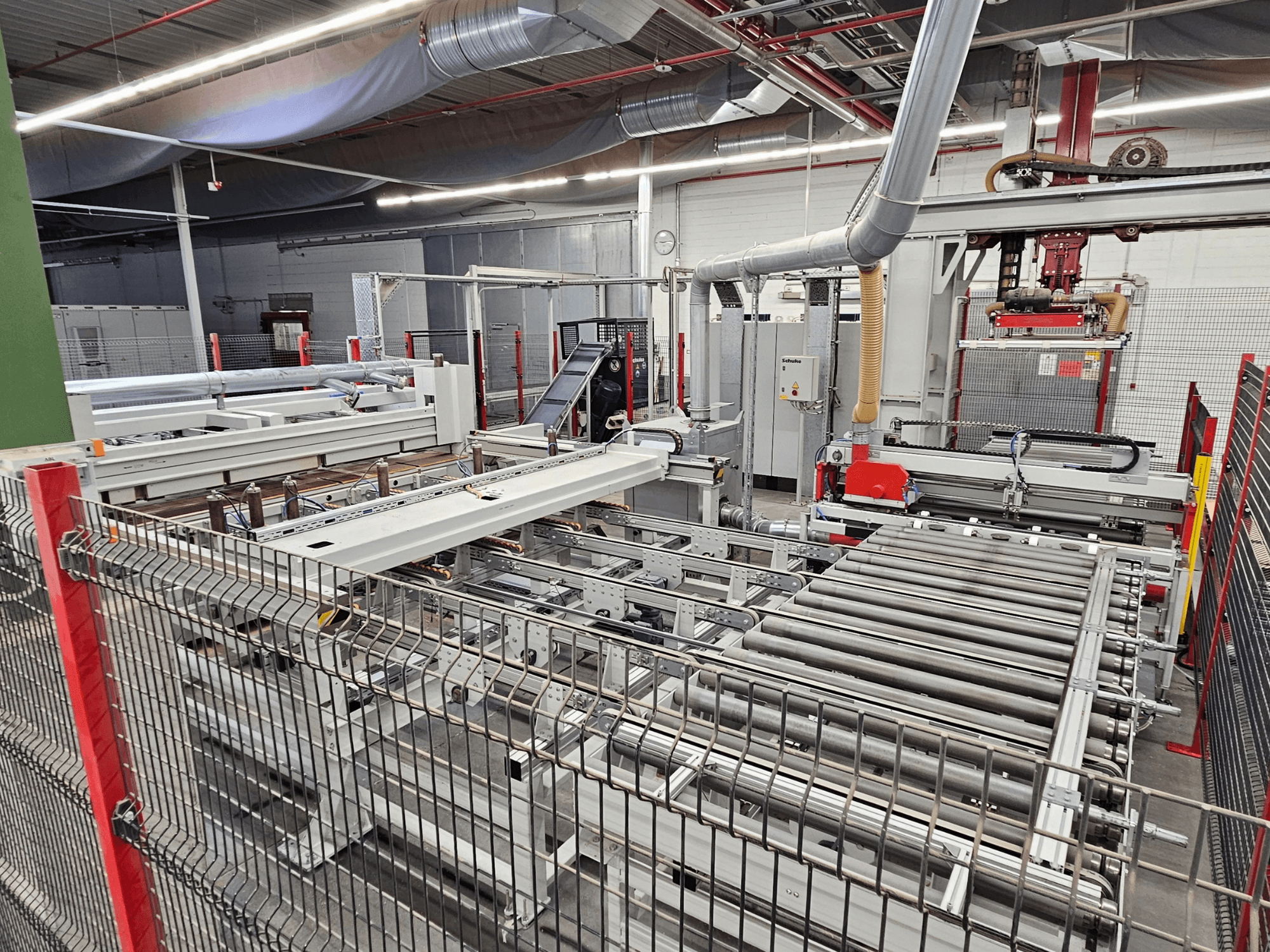 Serra de painel HOLZMA HPP81-3200 mostrada numa vista frontal, com rolos transportadores e componentes de máquinas numa oficina.