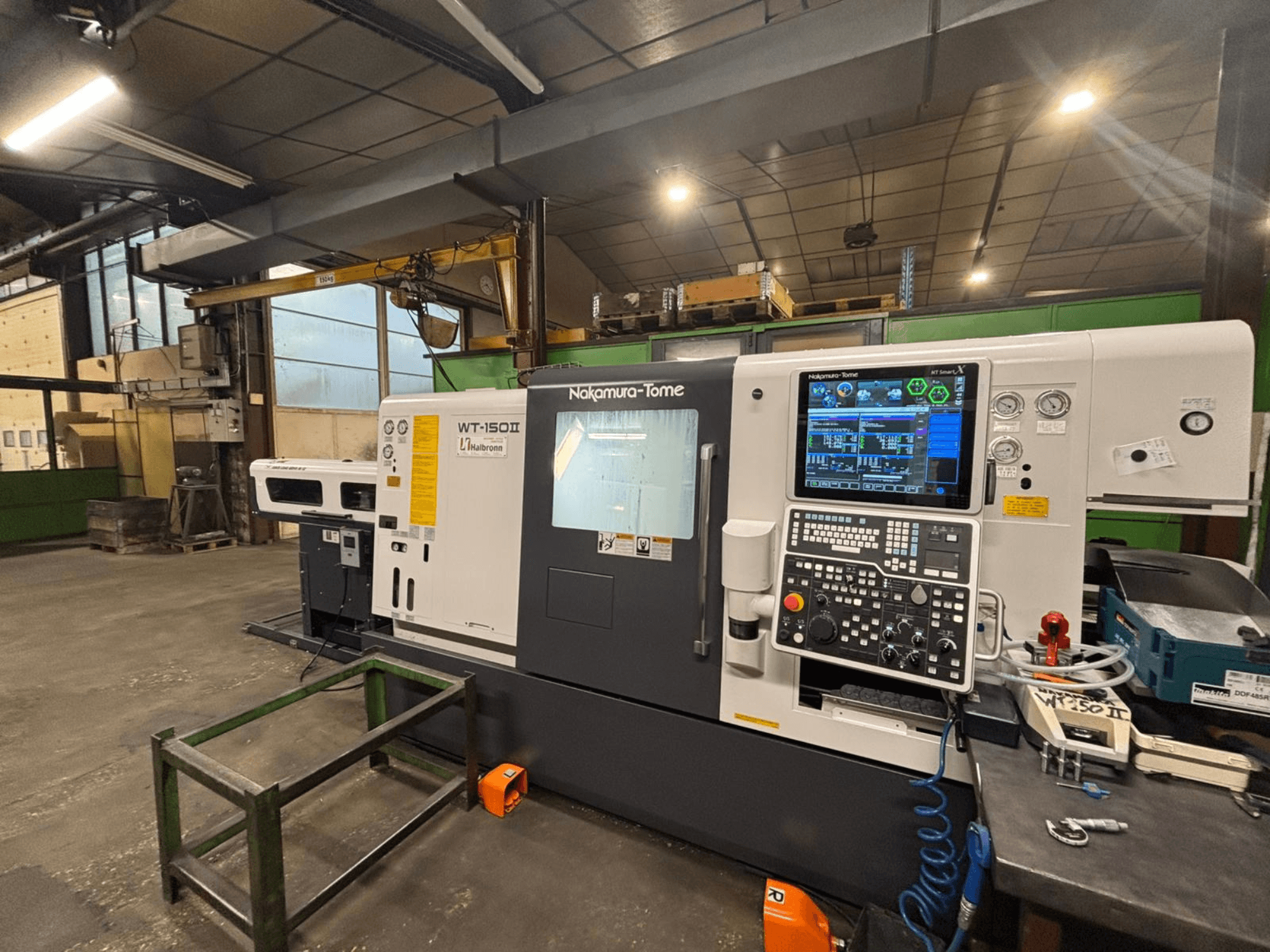 Máquina Nakamura-Tome WT-150II, vista frontal, com painel de controlo e ferramentas visíveis numa bancada de trabalho numa oficina.