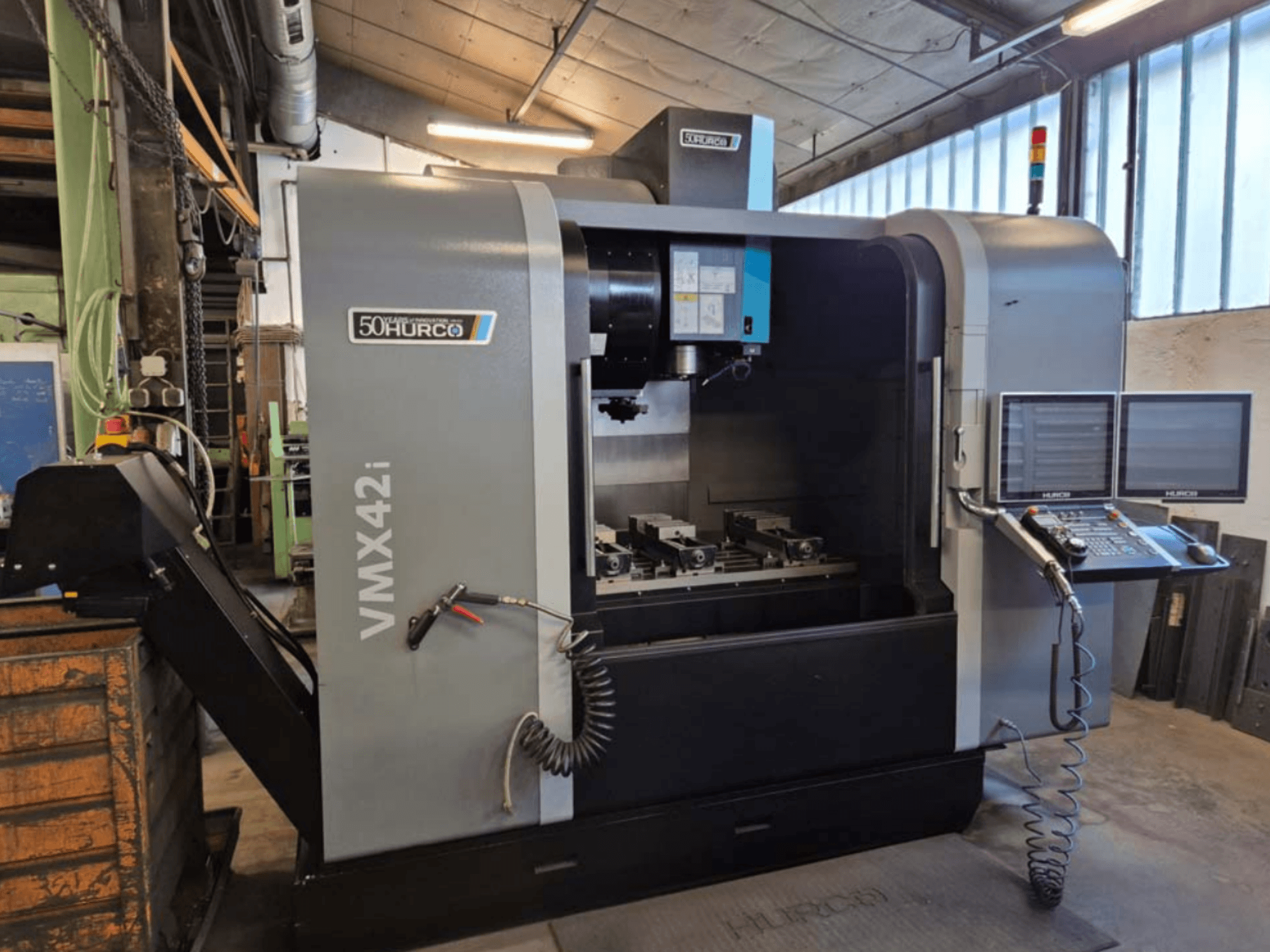 Centro de maquinação vertical Hurco VMX 42i, vista frontal, mostrando o painel de controlo e a área de trabalho com tornos.