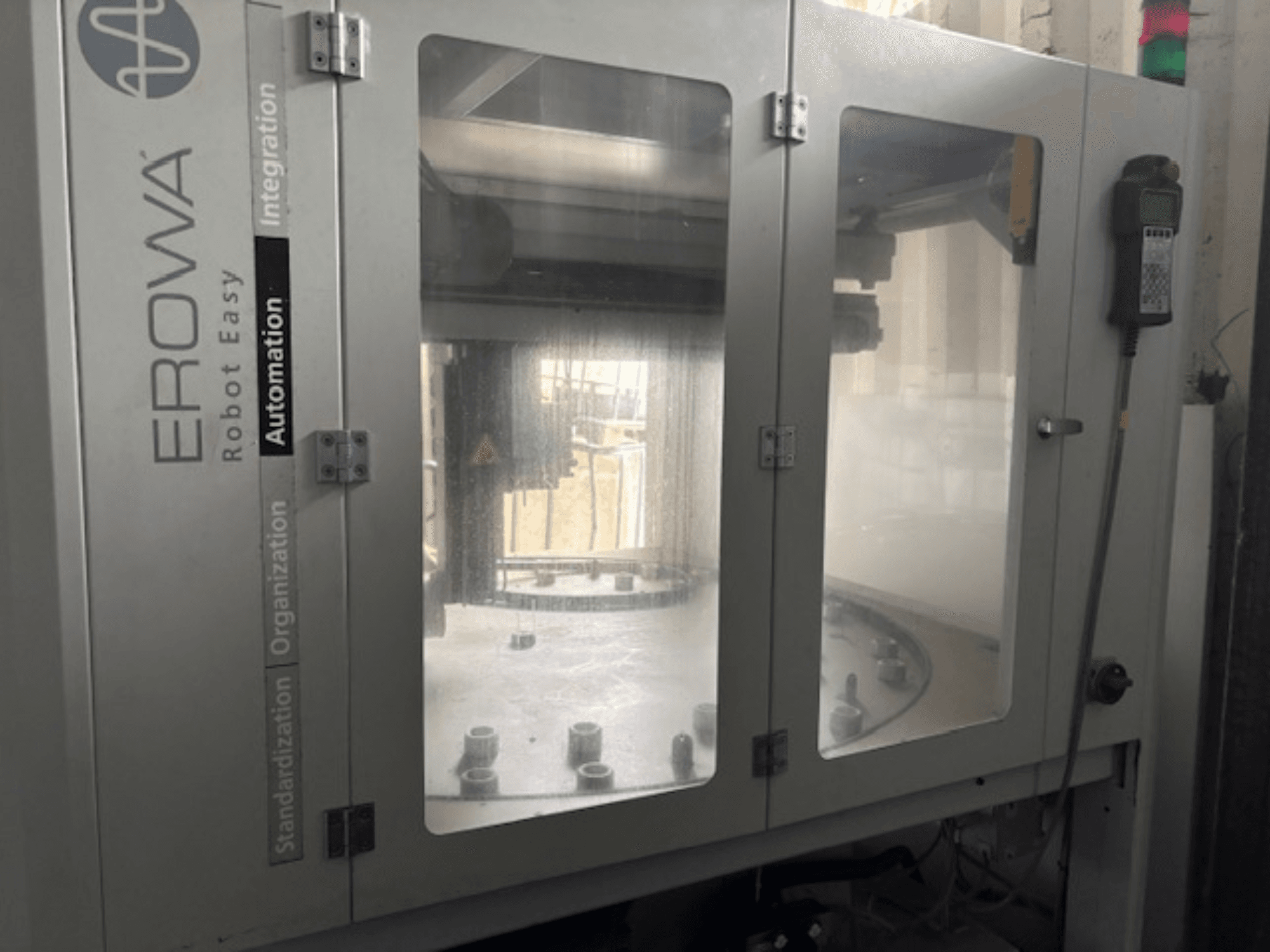 Vista frontal do EROWA Robot Easy Automation; apresenta portas transparentes, componentes de automação visíveis e painel de controlo.