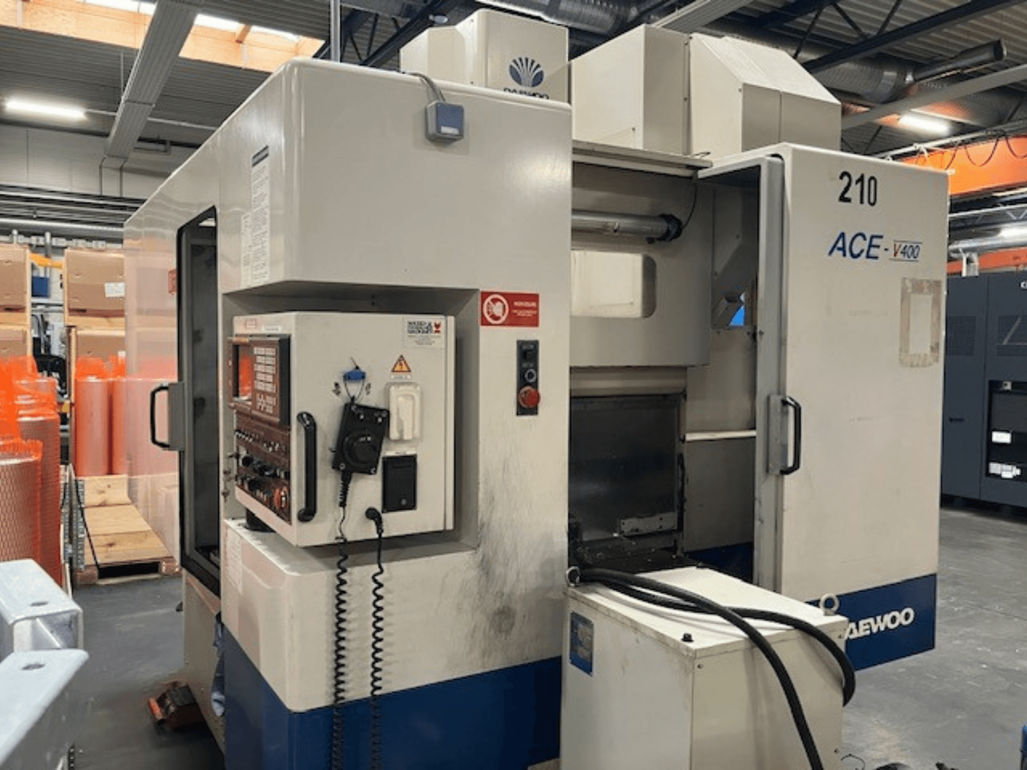 Máquina CNC Daewoo ACE-V400 em vista lateral, com painel de controlo, tanque de refrigeração e área de trabalho aberta.