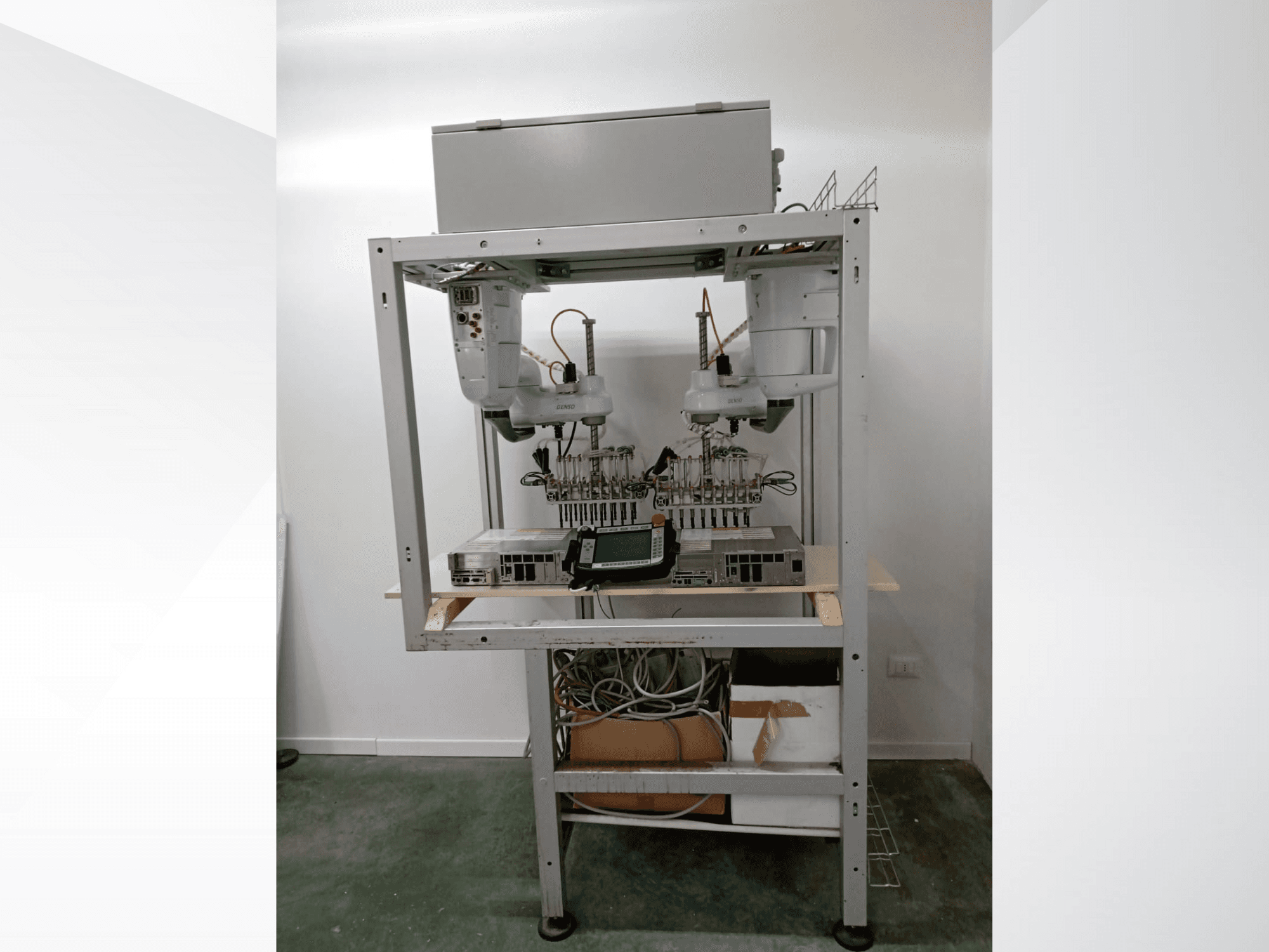 Estação de trabalho robótica automatizada com dois braços, unidade de visualização e eletrónica numa estrutura metálica, vista frontal, configuração de tecnologia avançada.