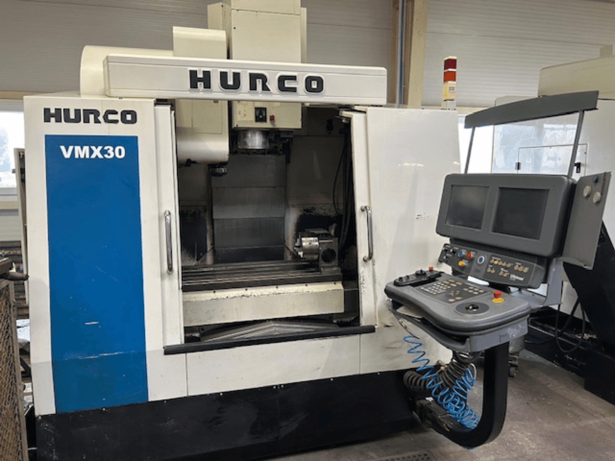 Fresadora CNC Hurco VMX30 numa oficina, vista frontal; possui painel de controlo com dois ecrãs e botões operacionais.