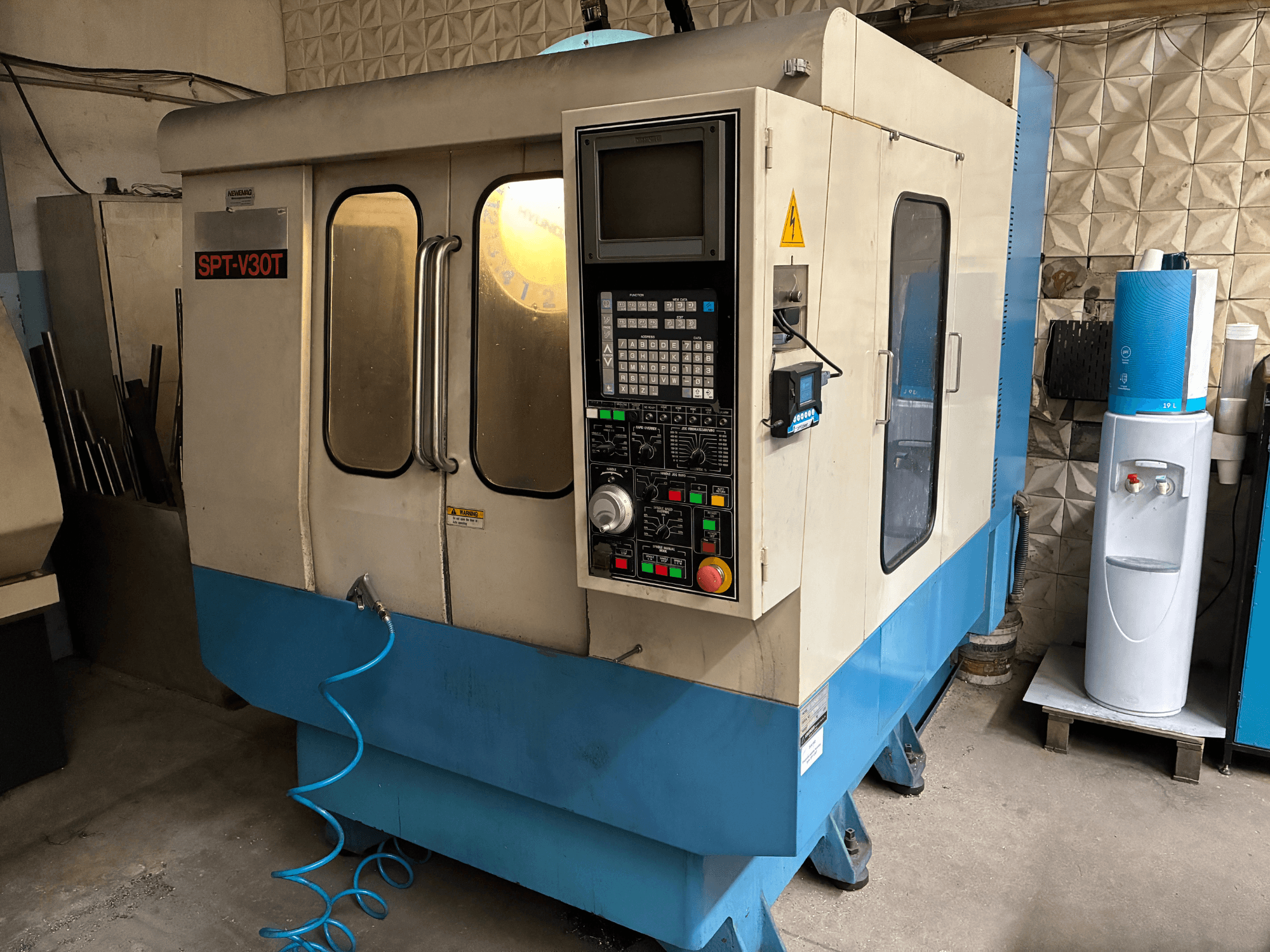 Máquina CNC SPT-V30T em azul e branco, vista frontal com painel de controlo, portas e mangueira de ar. Ideal para maquinagem de precisão.