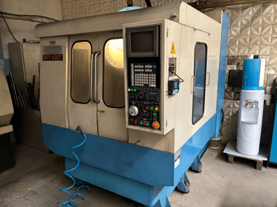 Máquina CNC SPT-V30T em azul e branco, vista frontal com painel de controlo, portas e mangueira de ar. Ideal para maquinagem de precisão.