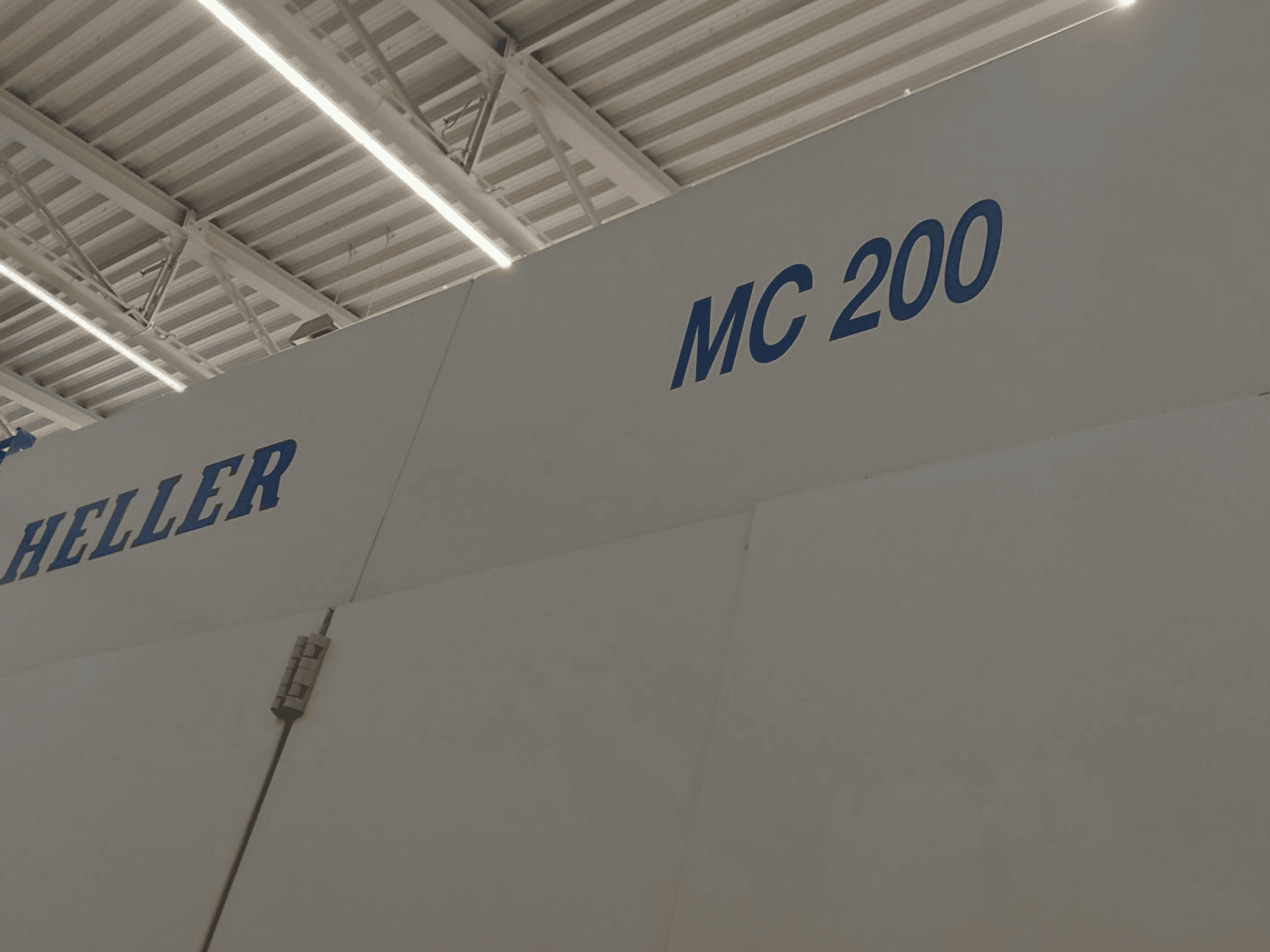 Centro de maquinação horizontal Heller MC 200, mostrado de lado, destacando a marca e o modelo em letras azuis numa superfície branca.