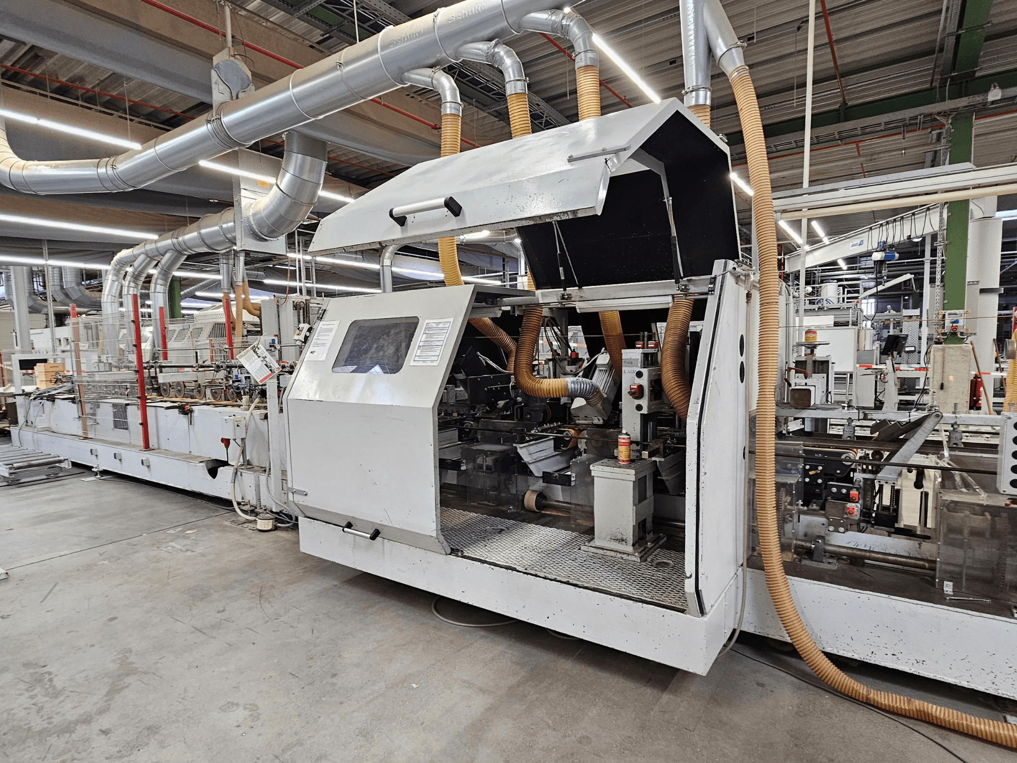 Lixadora de bordos HOMAG FG63 em fábrica, vista lateral mostrando os componentes operacionais e o sistema de extração de poeiras.