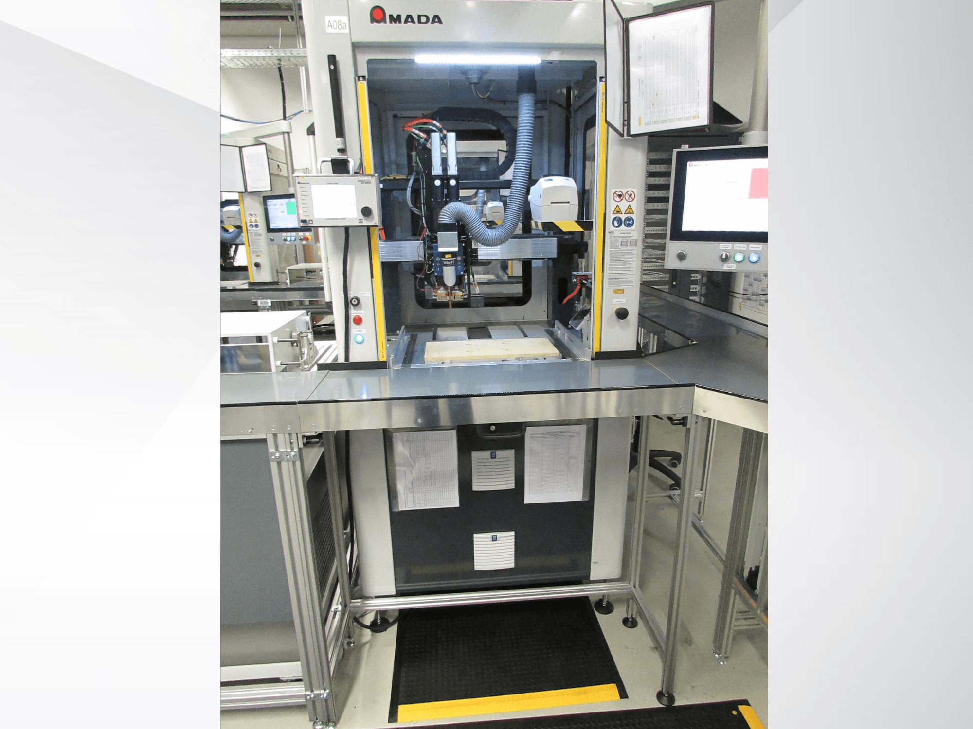 Vista frontal da máquina de automação AMADA Jupiter System, com painel de controlo, monitor e área de trabalho desimpedida para a operação.