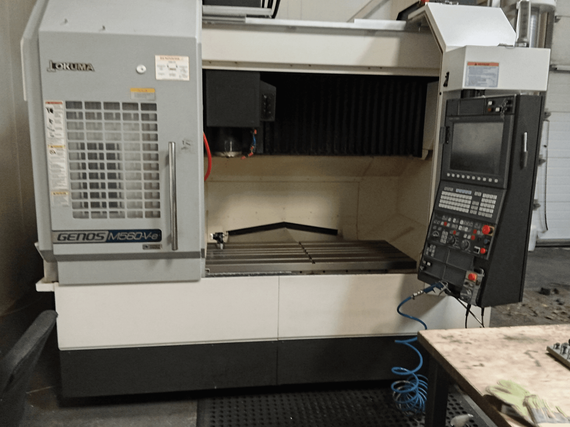 Okuma GENOS M560-V, vista frontal de um centro de maquinação vertical com painel de controlo, interface CNC e área de corte visível.