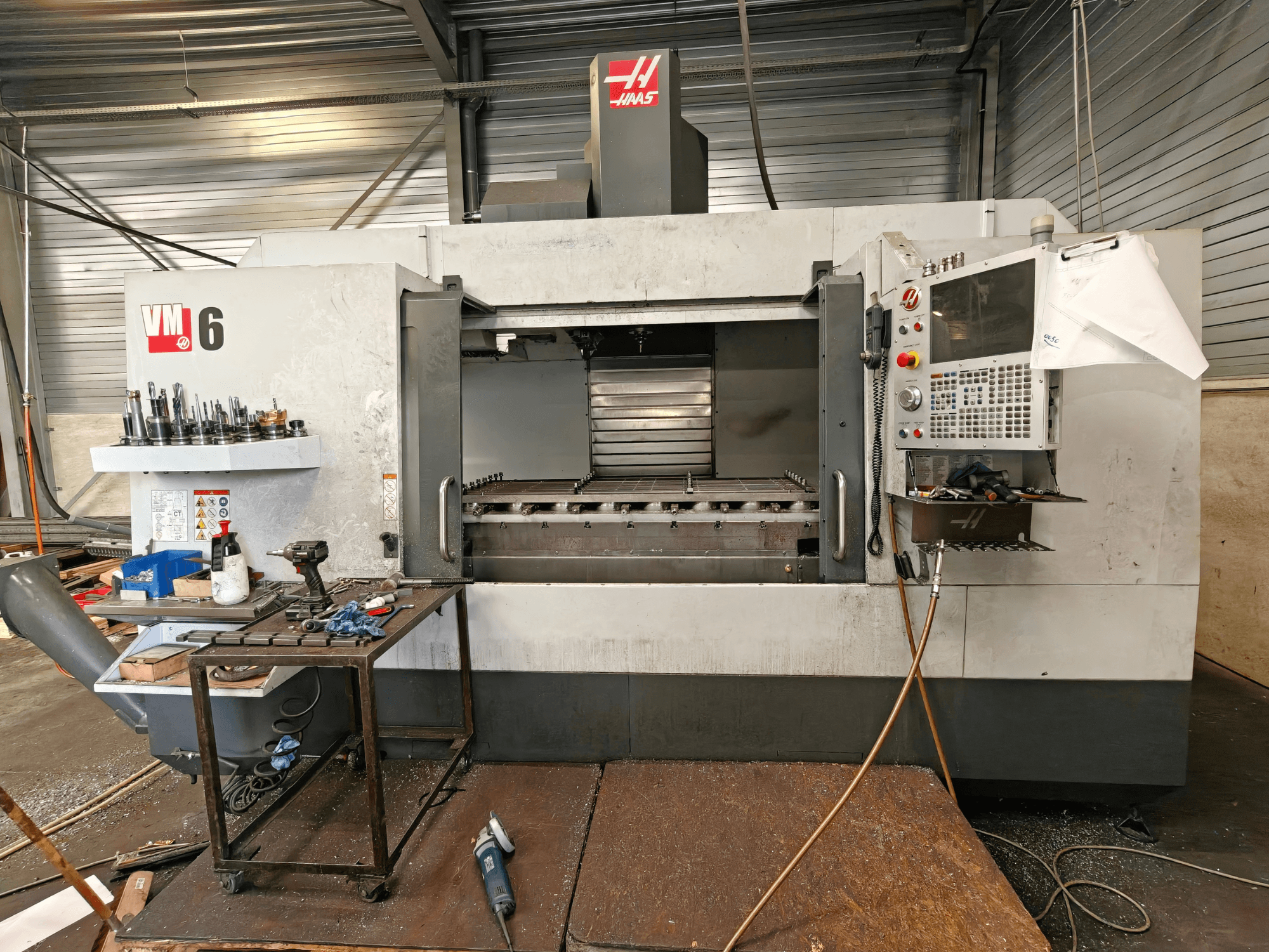 Centro de maquinagem vertical Haas VM-6, vista frontal, com o armazém de ferramentas, o painel de controlo e os resíduos na área de trabalho visíveis.