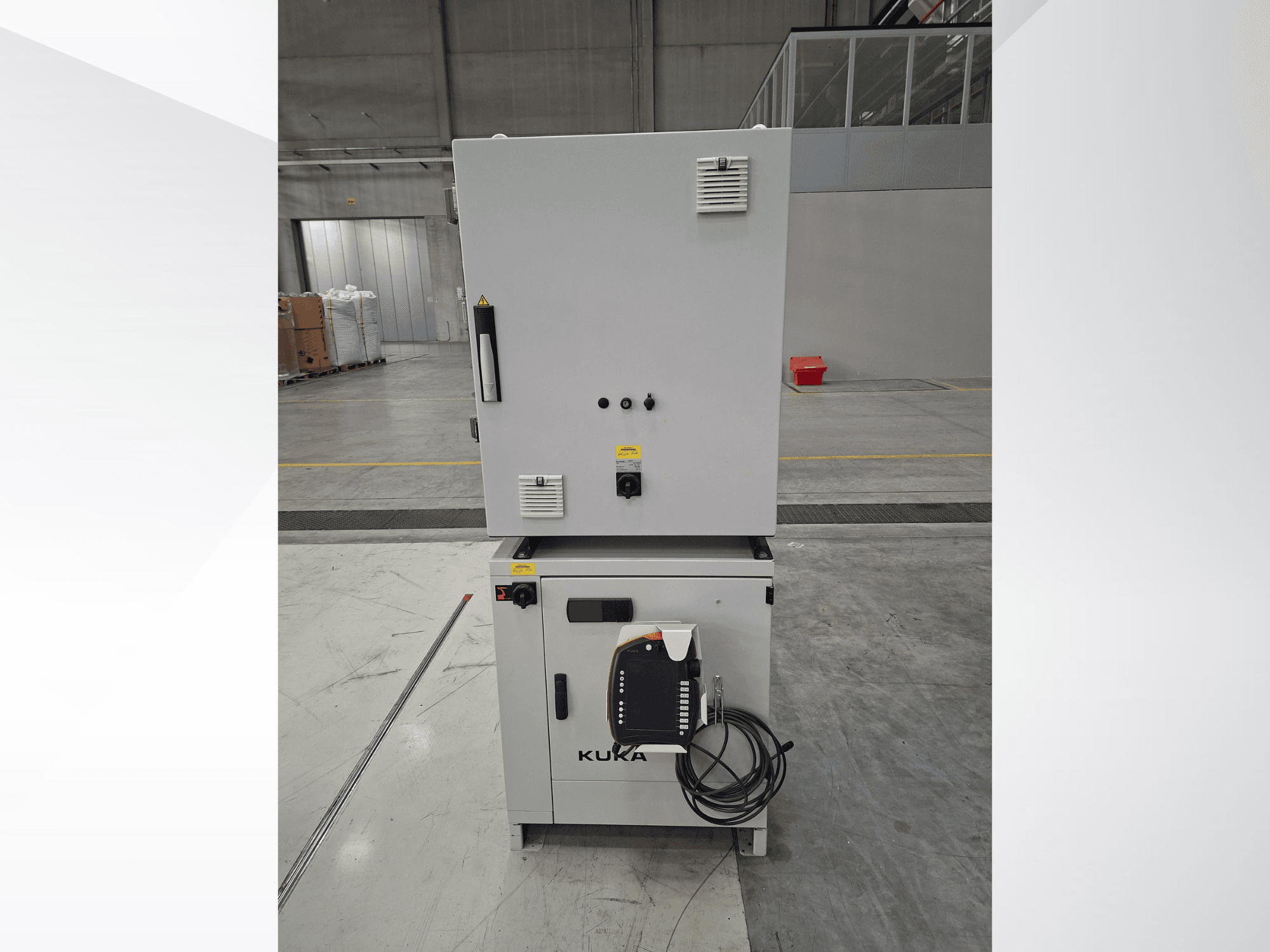Controlador do braço robótico KUKA KR 90 R2700 PRO C4 FLR, vista frontal que mostra o painel de controlo e as etiquetas de segurança num armazém espaçoso.