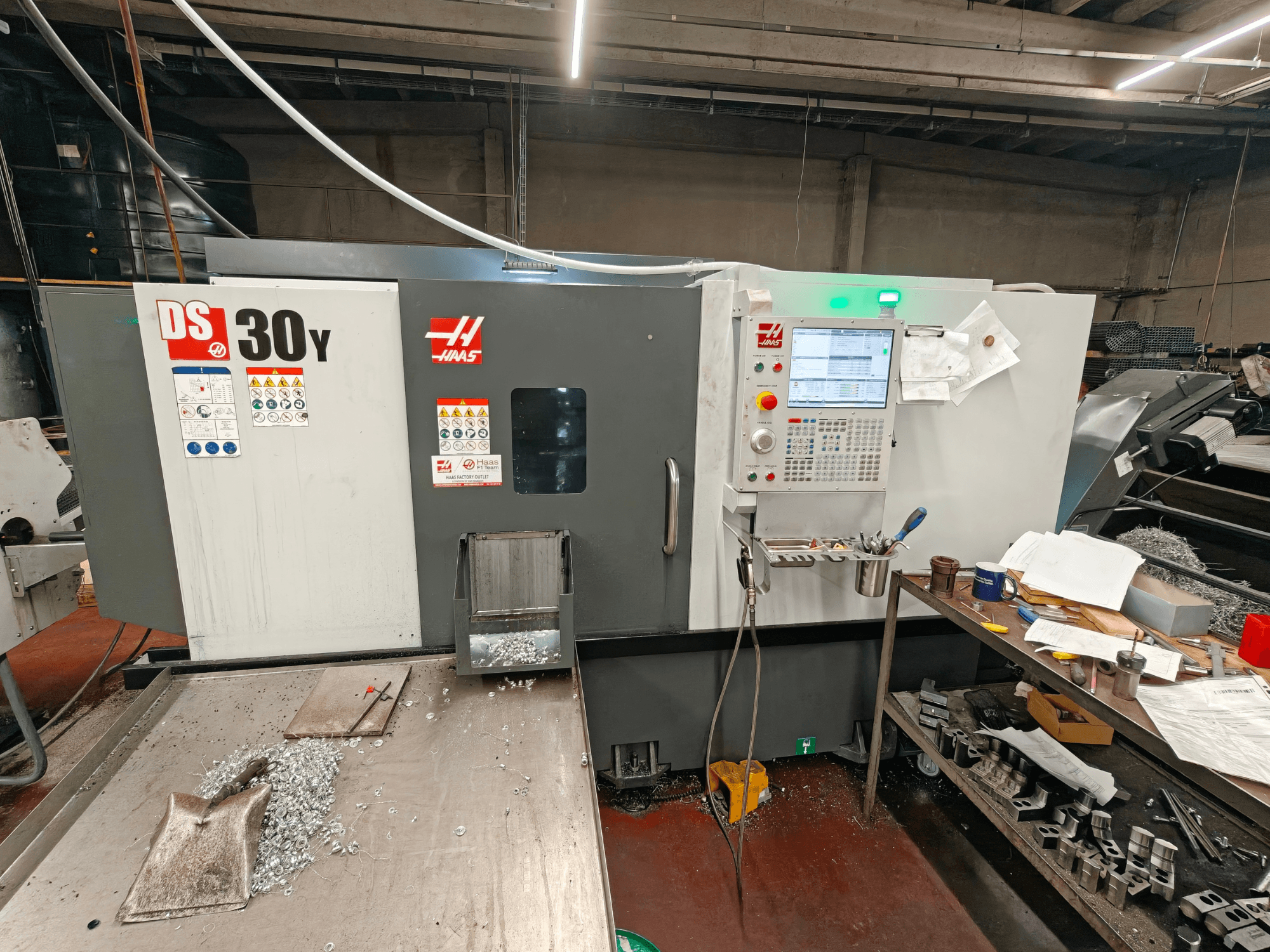 Torno horizontal HAAS DS30Y numa oficina, vista frontal que mostra o painel de controlo e limalhas de metal na superfície.