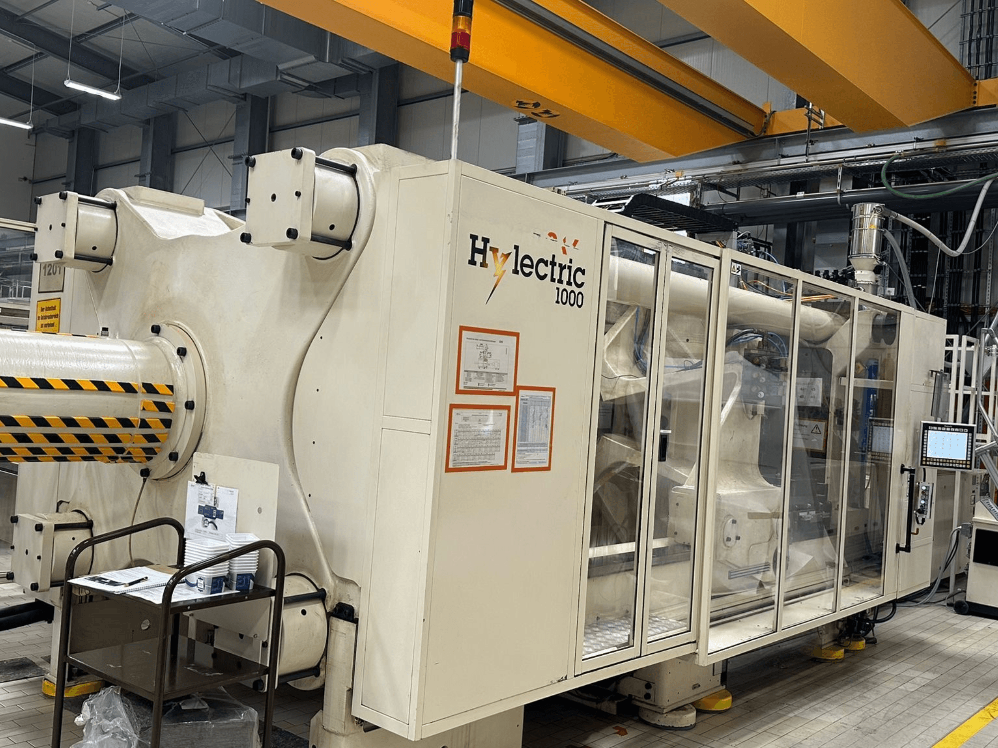 Máquina de moldagem por injeção elétrica Husky Hylelectric H1000 RS95/80, vista lateral com o painel de controlo e os dispositivos de segurança visíveis.