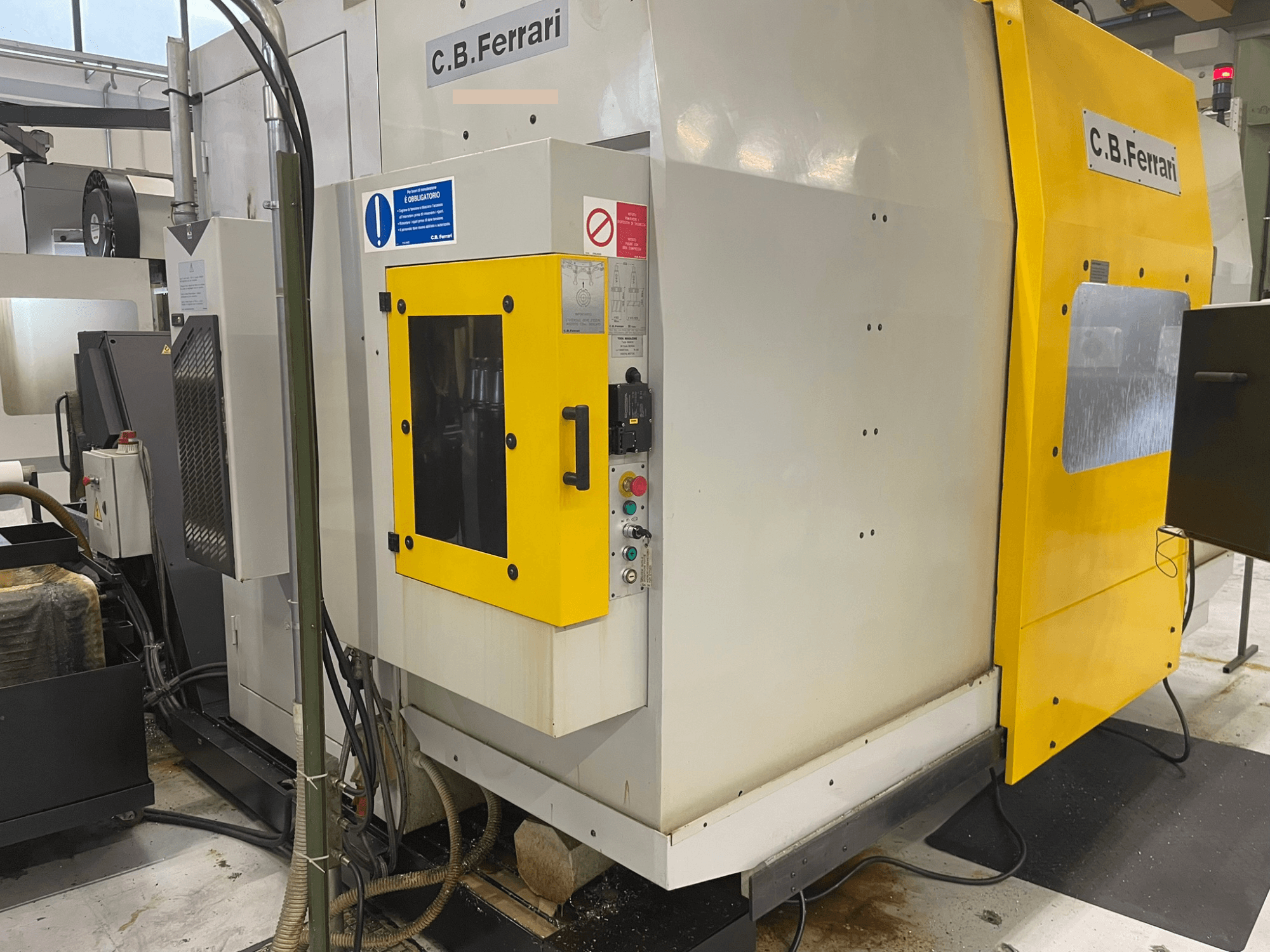 Máquina industrial C.B. Ferrari, vista frontal; porta amarela, painel de controlo e componentes de maquinagem visíveis.