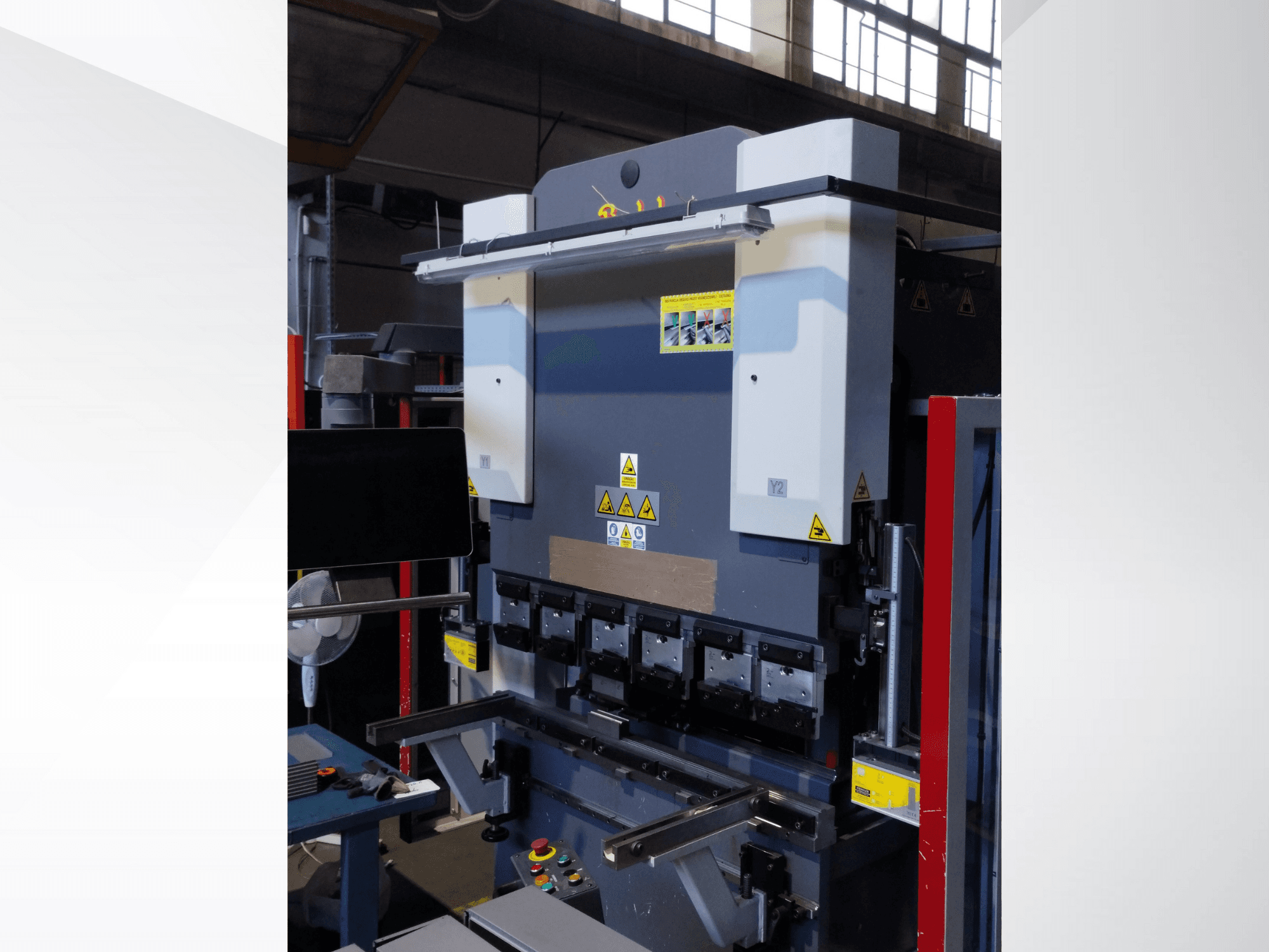 Máquina de prensagem a frio, vista frontal. Possui controlos visíveis, autocolantes de segurança e vários suportes de moldes para uma dobragem de precisão.