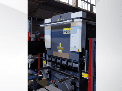 Máquina de prensagem a frio, vista frontal. Possui controlos visíveis, autocolantes de segurança e vários suportes de moldes para uma dobragem de precisão.
