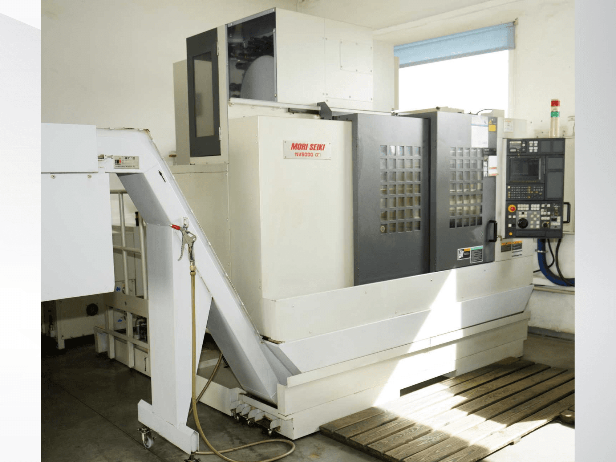 Centro de maquinagem vertical MORI SEIKI NV 5000 alpha1, visto de frente, mostrando o painel de controlo, as características de segurança e a área de carregamento.