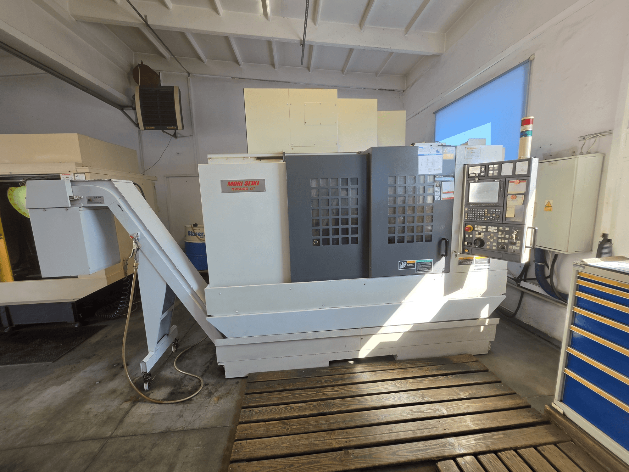 Centro de usinagem vertical MORI SEIKI NV 5000 alpha1, vista frontal que mostra o painel de controlo e as características da máquina num ambiente de oficina.