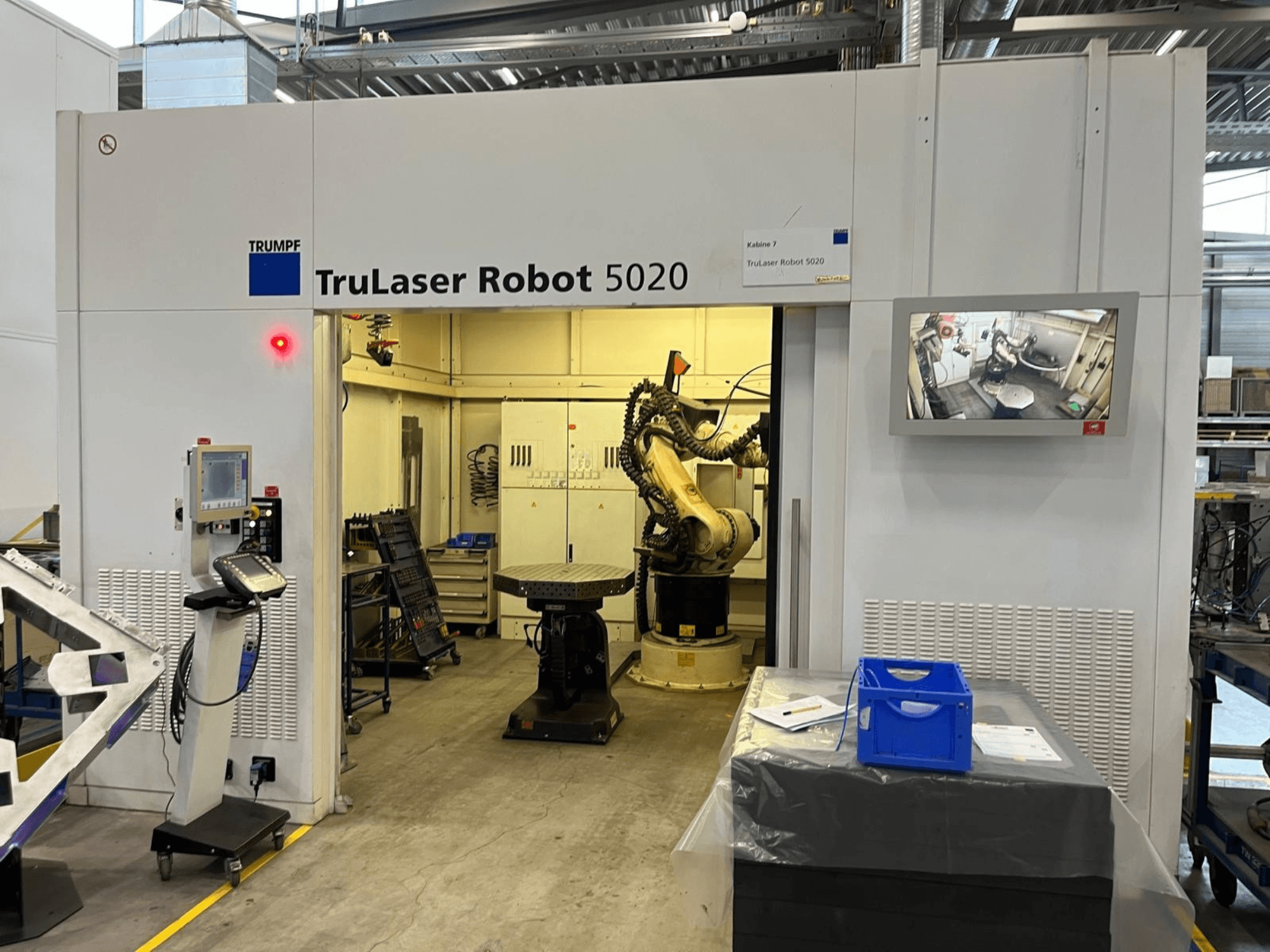 TRUMPF TruLaser Robot 5020 num ambiente industrial, com os painéis de comando, um braço robótico e um monitor que exibe as operações.