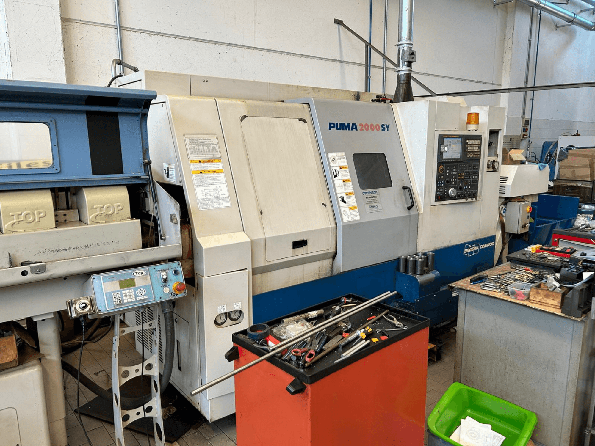 Torno horizontal DOOSAN PUMA 2000SY numa oficina, vista lateral que mostra o painel de controlo e as ferramentas nas proximidades.