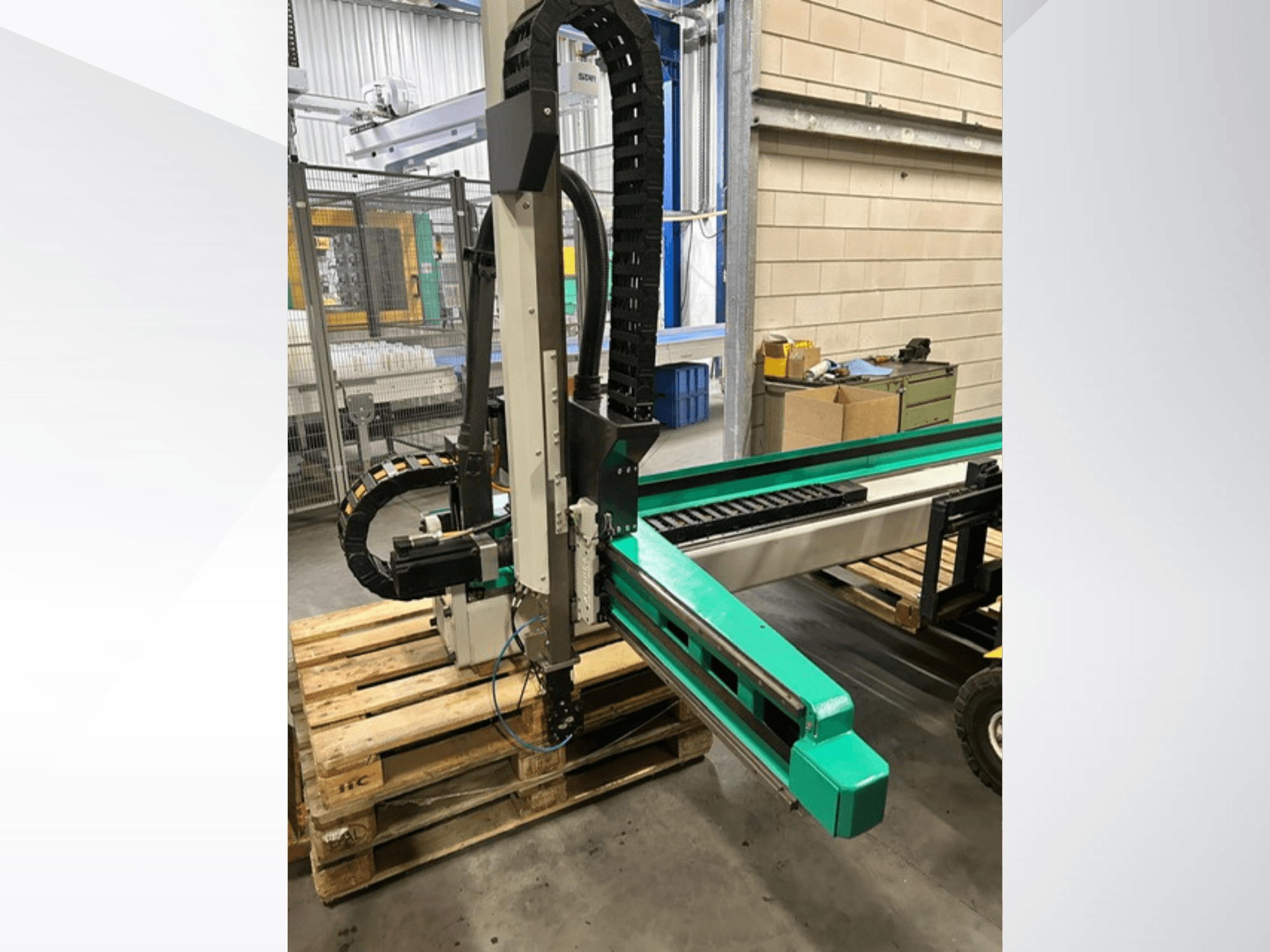 Arburg Multilift Select 15kg quer, vista lateral do sistema de manuseamento de peças de trabalho em paletes de madeira, mostrando o braço robótico e os componentes de controlo.