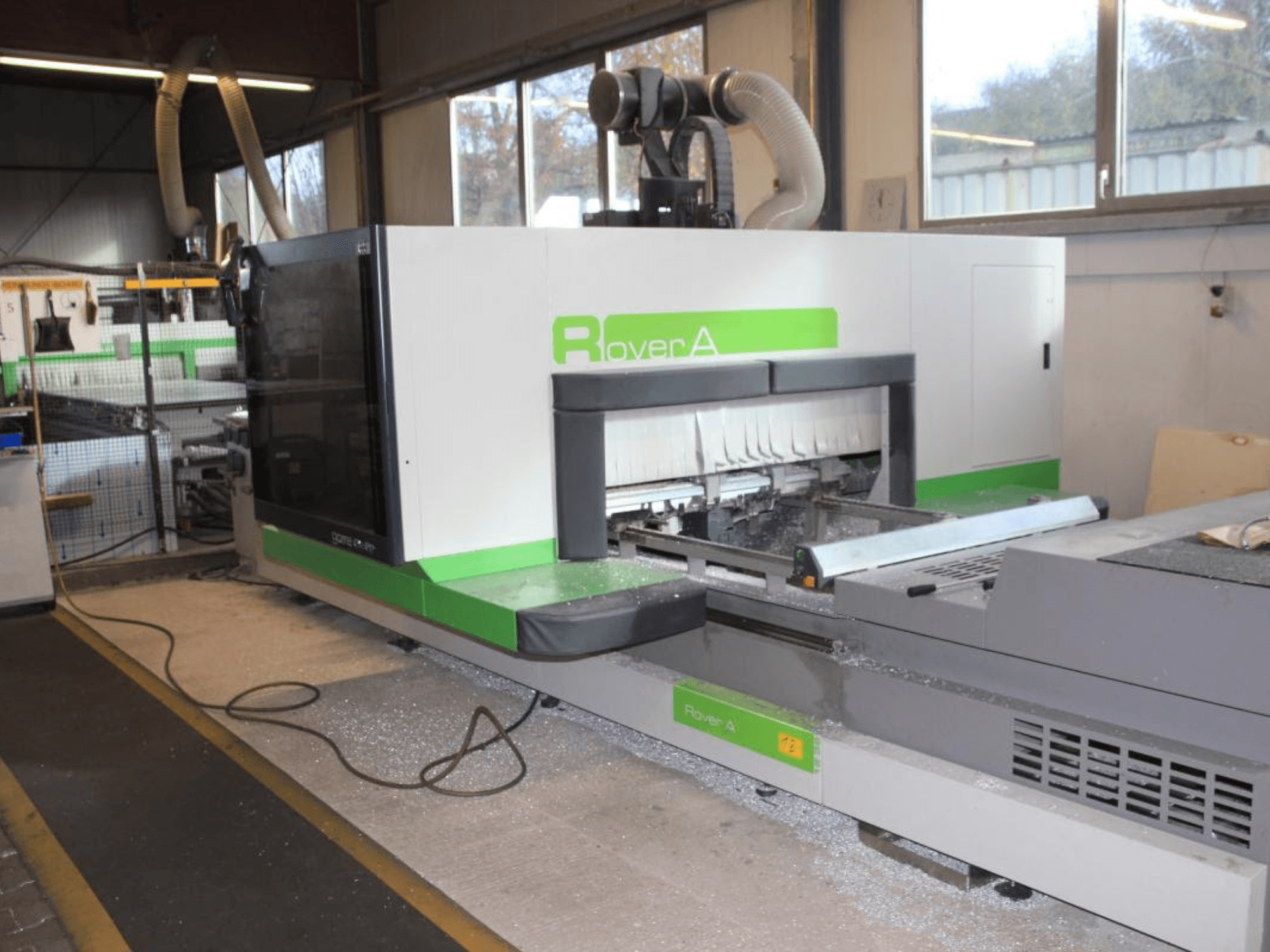 BIESSE Rover A 1232 CNC router, vista lateral mostrando a área de corte e o painel de controlo num ambiente industrial.
