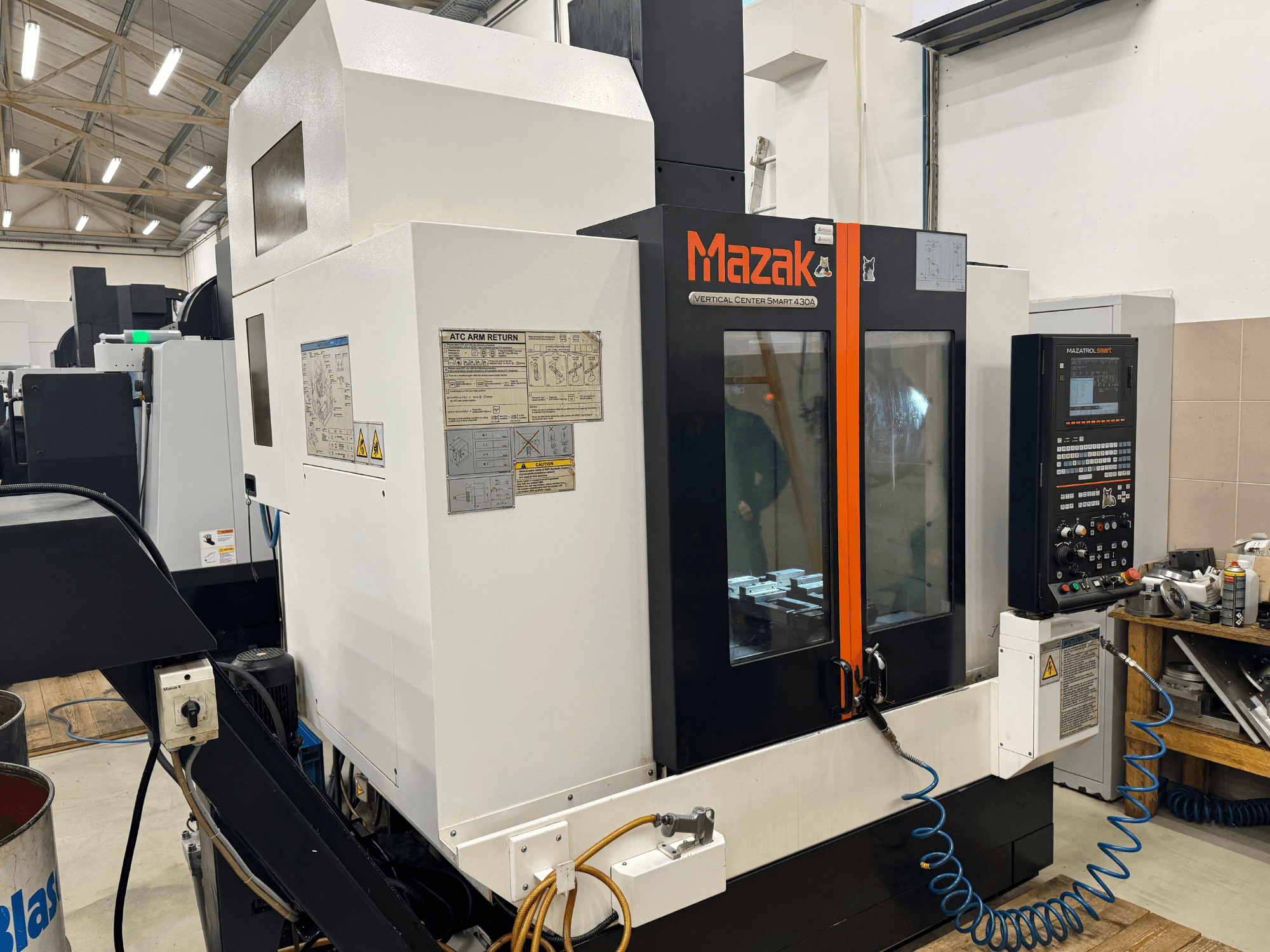 Mazak Vertical Center Smart 430A, vista frontal; fresadora CNC com painel de controlo, caixa transparente e suporte de ferramentas visível.