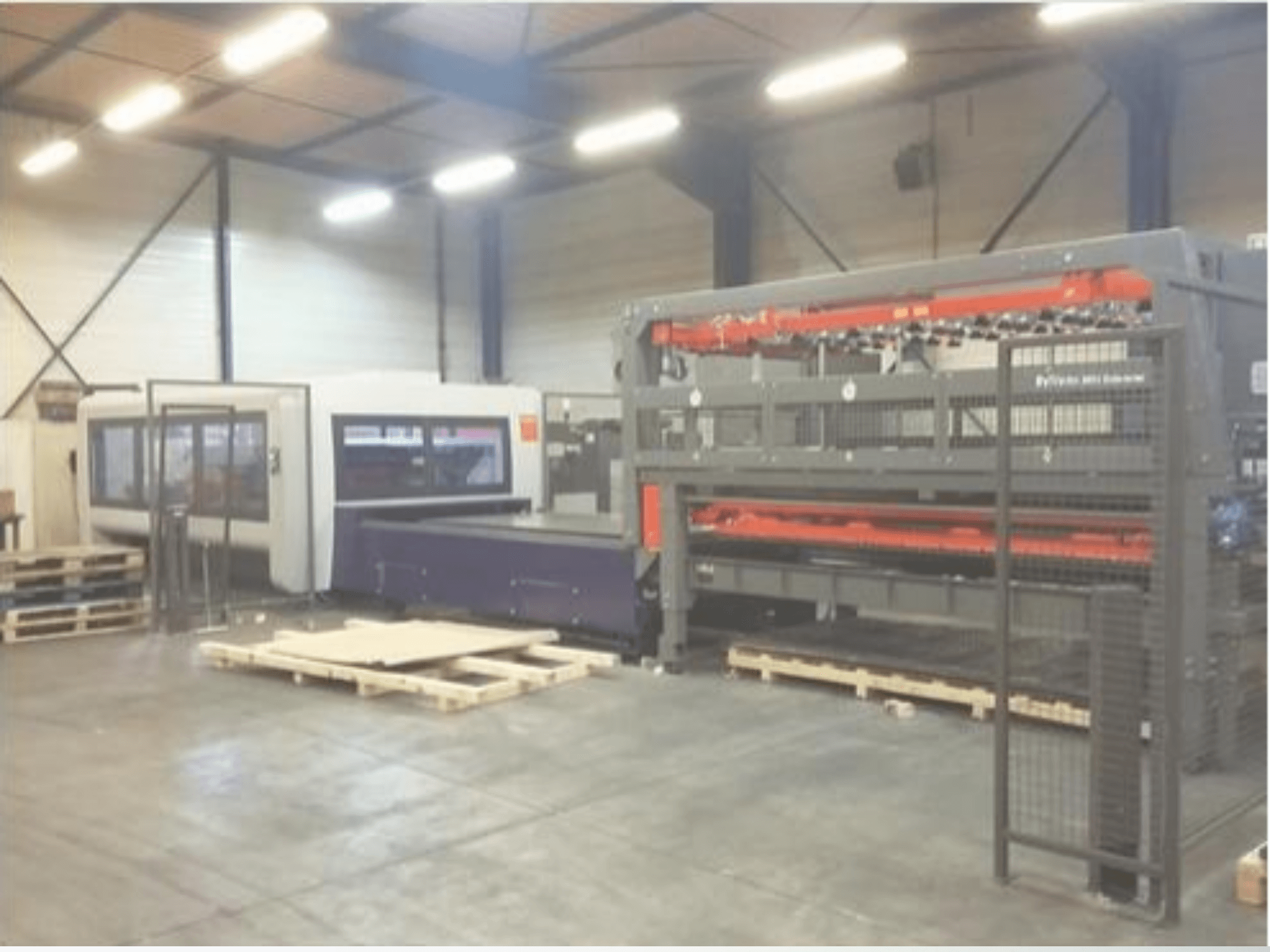 Instalação de maquinaria industrial num armazém; inclui um cortador laser cinzento e um router CNC roxo, vista frontal com paletes.