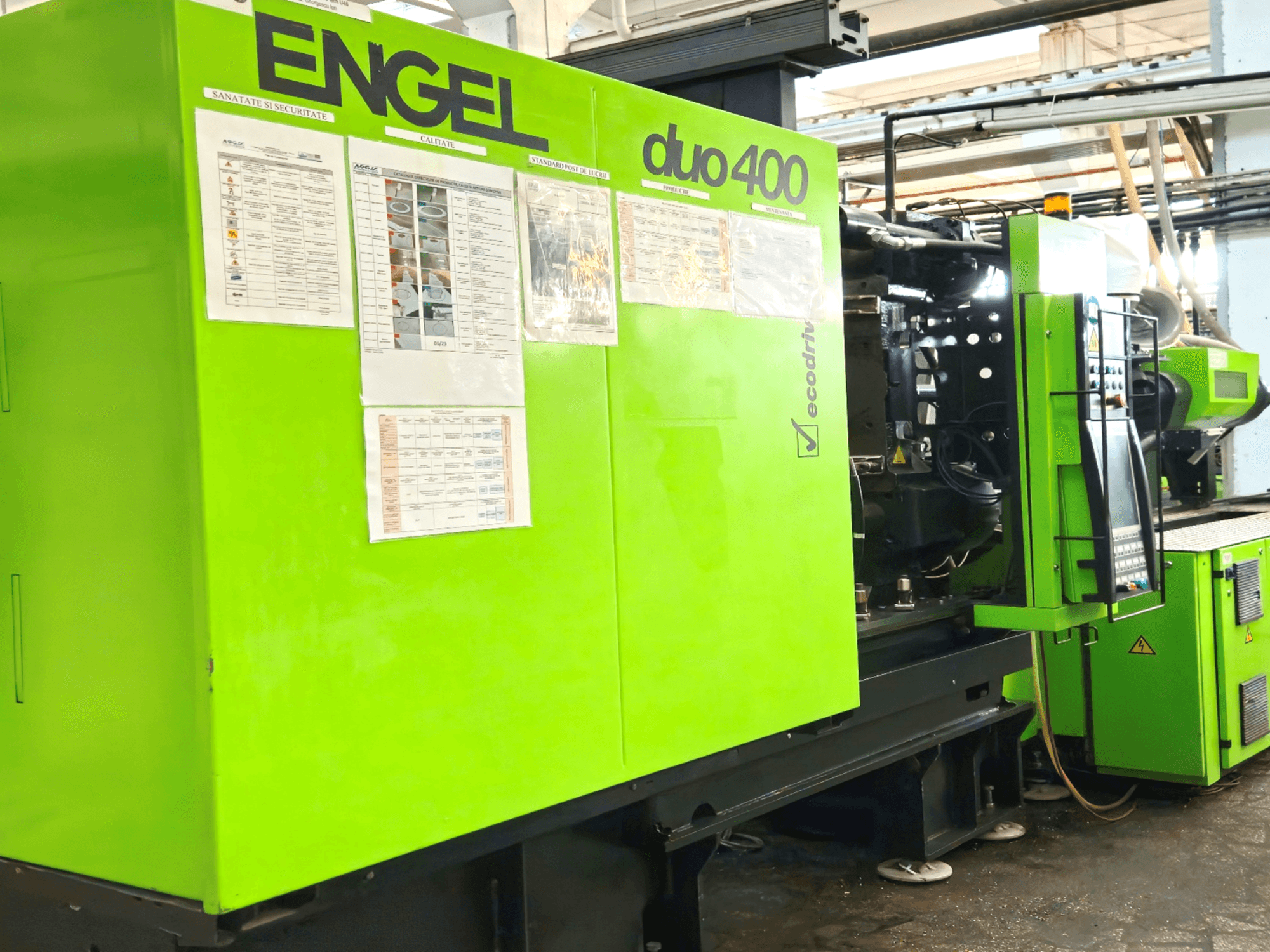 Máquina de moldagem por injeção ENGEL duo 400 verde, vista frontal, mostrando o painel de controlo e a documentação de segurança no exterior.