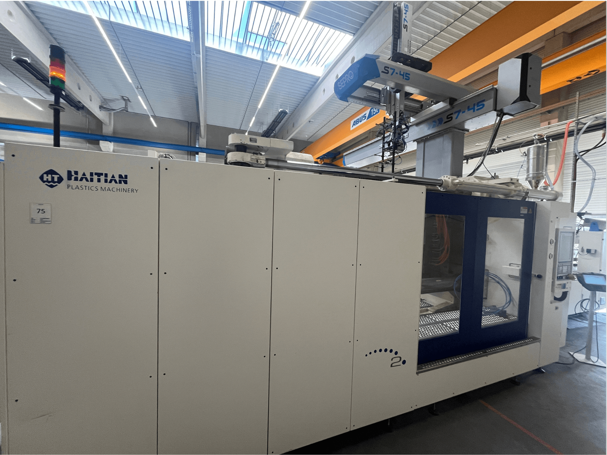 Máquina de moldagem por injeção Haitian S7-45 em vista lateral com painel de controlo e indicador luminoso de segurança. Design branco e azul.