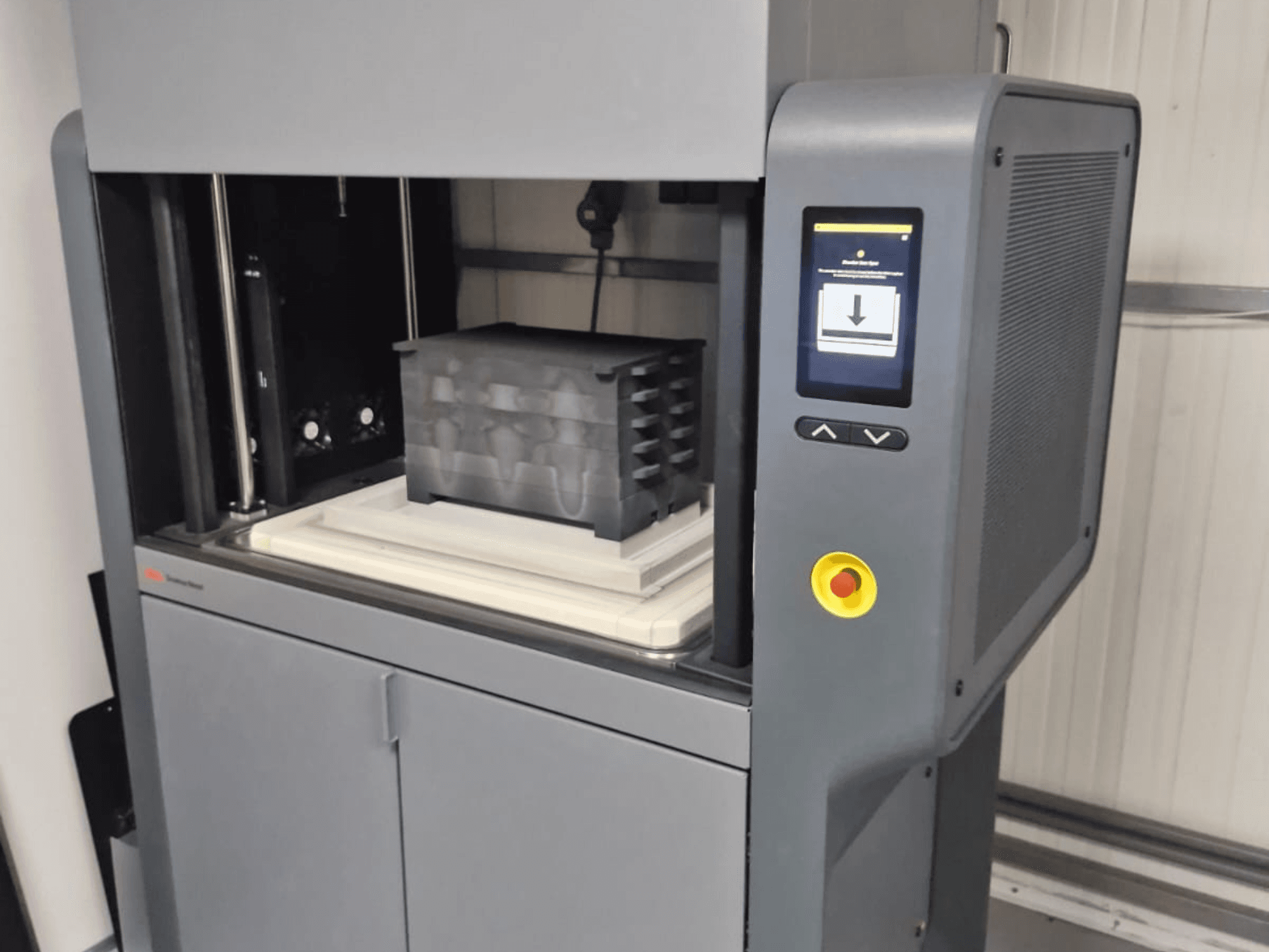 Impressora 3D Metal Studio 2 da Desktop Metal, vista frontal mostrando o painel de controlo e a base de impressão com um recipiente preto.