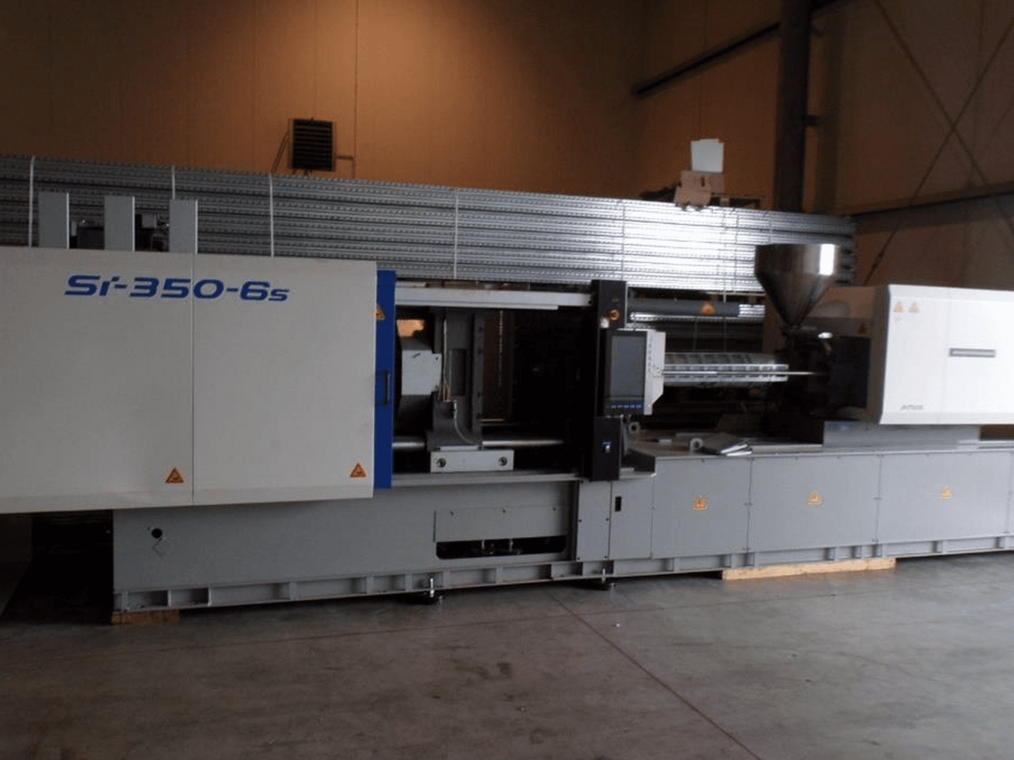 Máquina de moldagem por injeção Si-350-6s em vista lateral, com uma tremonha e um painel de controlo, situada num ambiente industrial espaçoso.