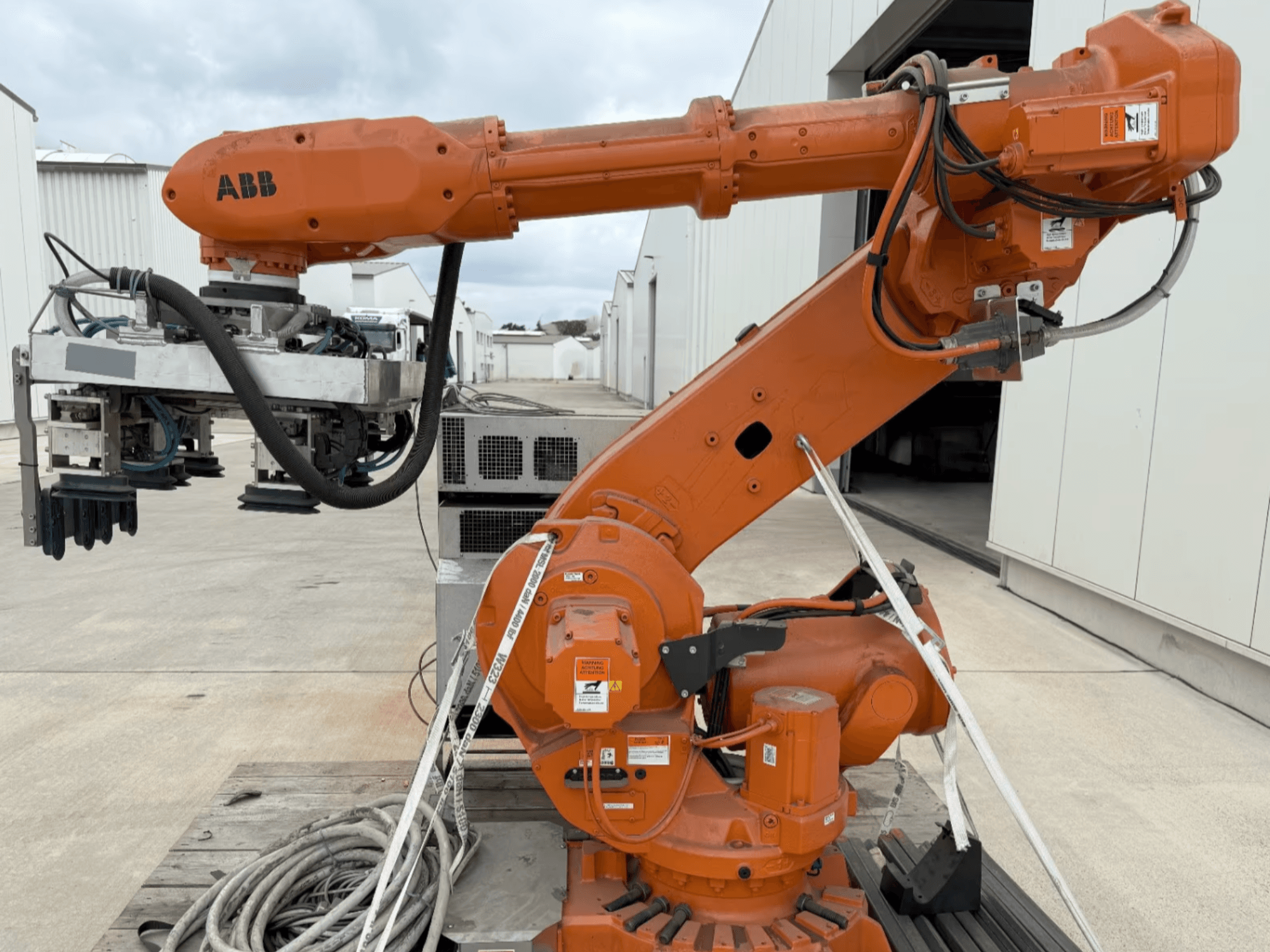 Braço robótico ABB RB 6600-130/3.2 em vista lateral, apresentando um braço robótico cor de laranja com um acessório de pinça e cablagem visível.