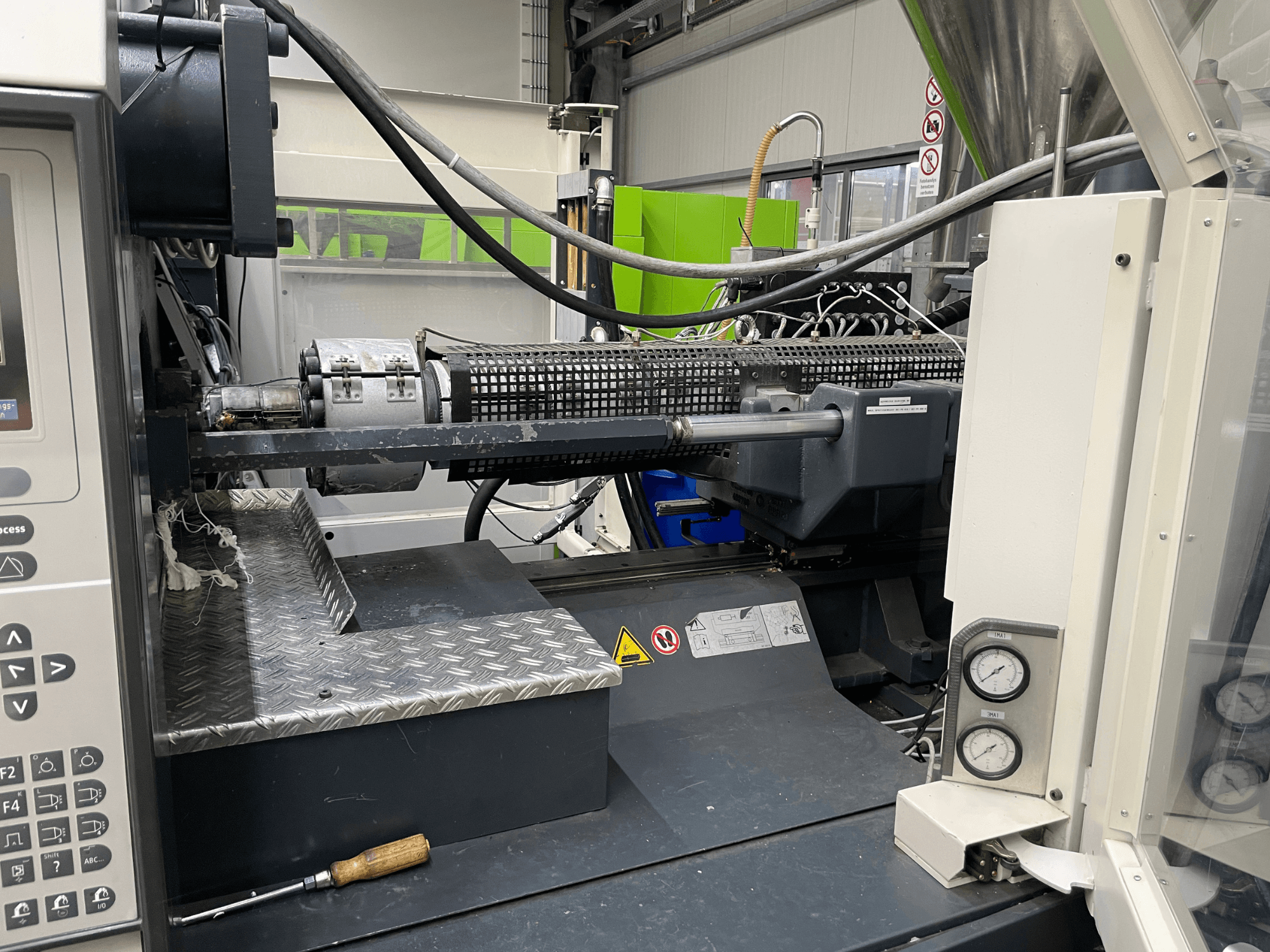 Vista lateral de uma máquina de moldagem por injeção com painel de controlo, extrusora e manómetros visíveis, ideal para tarefas de fabrico.